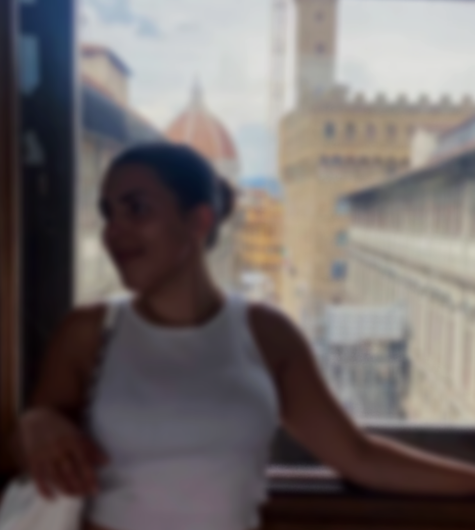 A woman sitting near a window with a cityscape view, including historic buildings and a dome, in Florence, Italy.