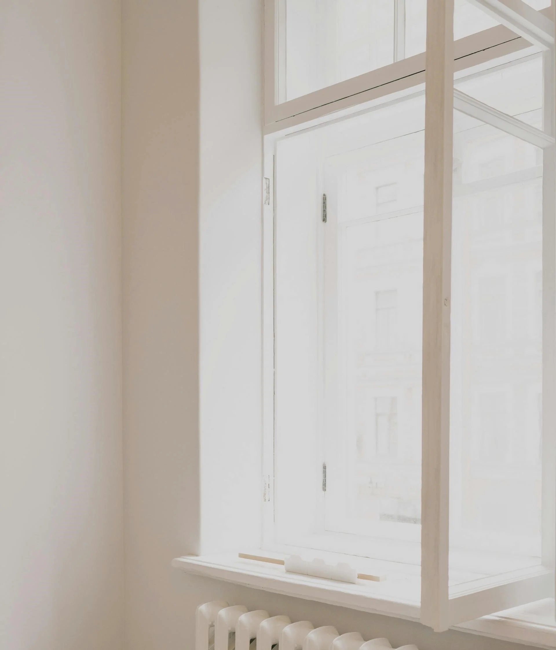 A white window with multiple glass panes and a windowsill, next to a white radiator, in a bright, minimalist room.