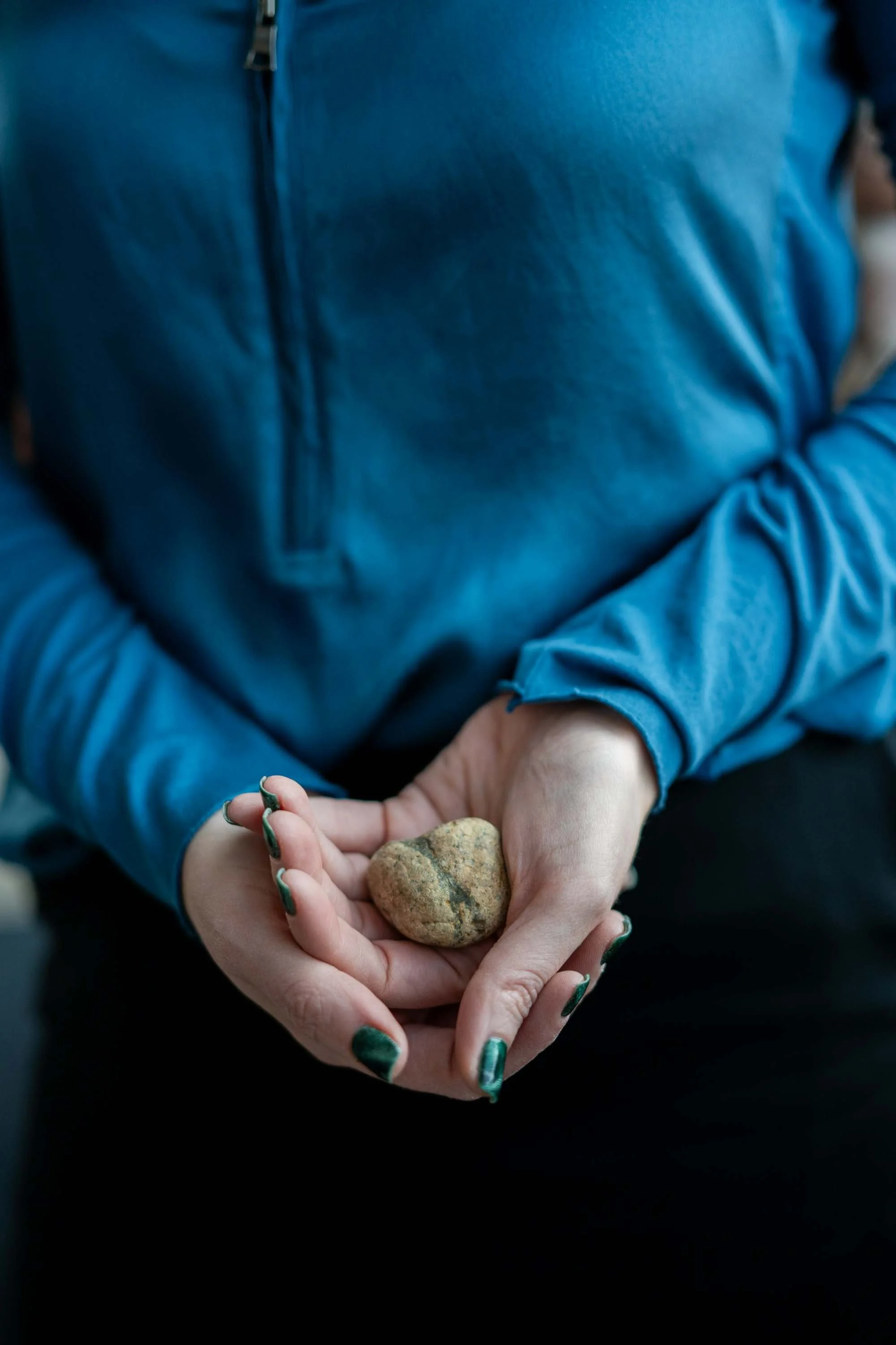 Person wearing a blue jacket holding a heart-shaped stone.