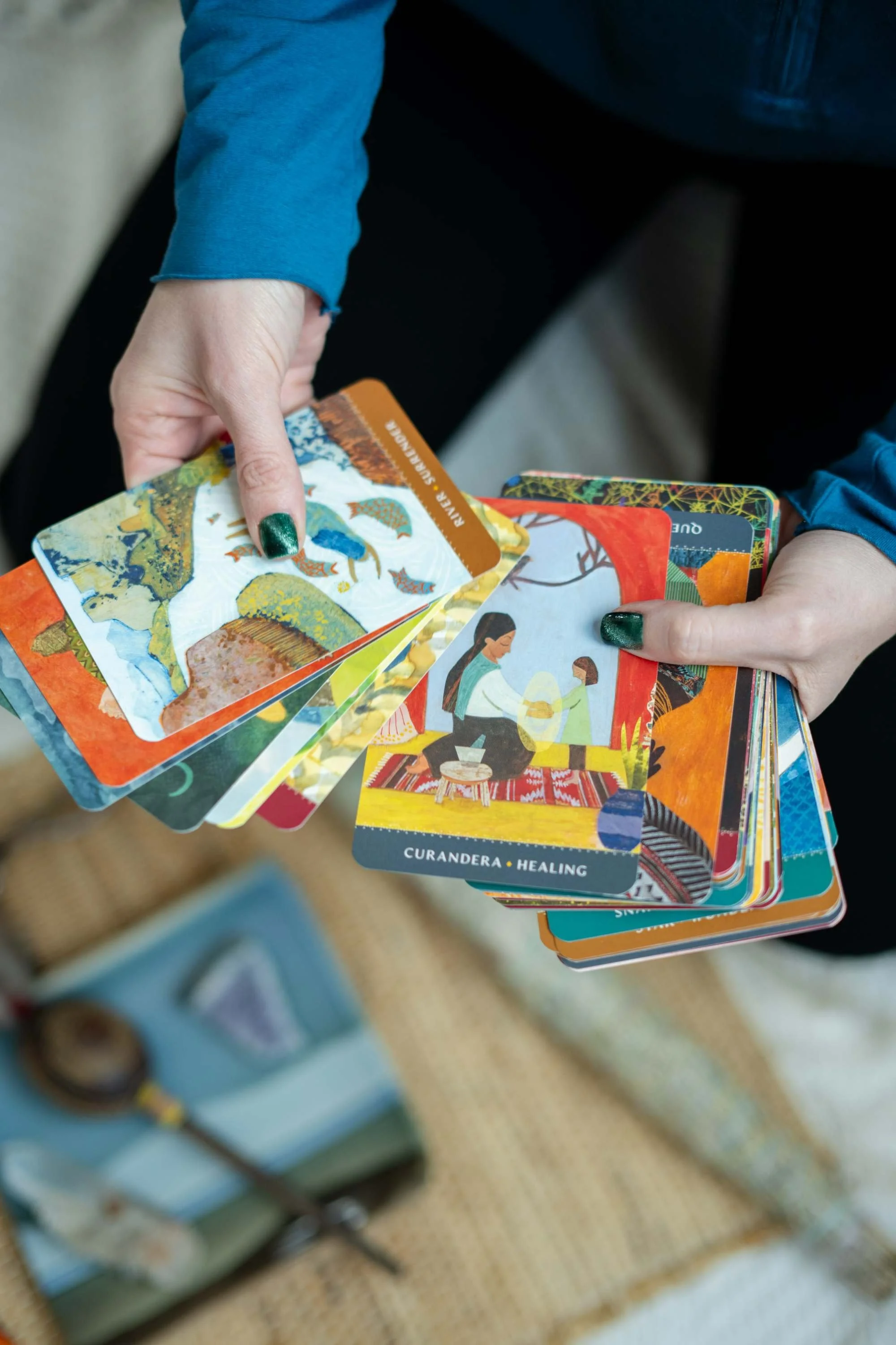 Person holding a colorful deck of tarot or oracle cards, with a focus on one card labeled 'Curandera - Healing'.