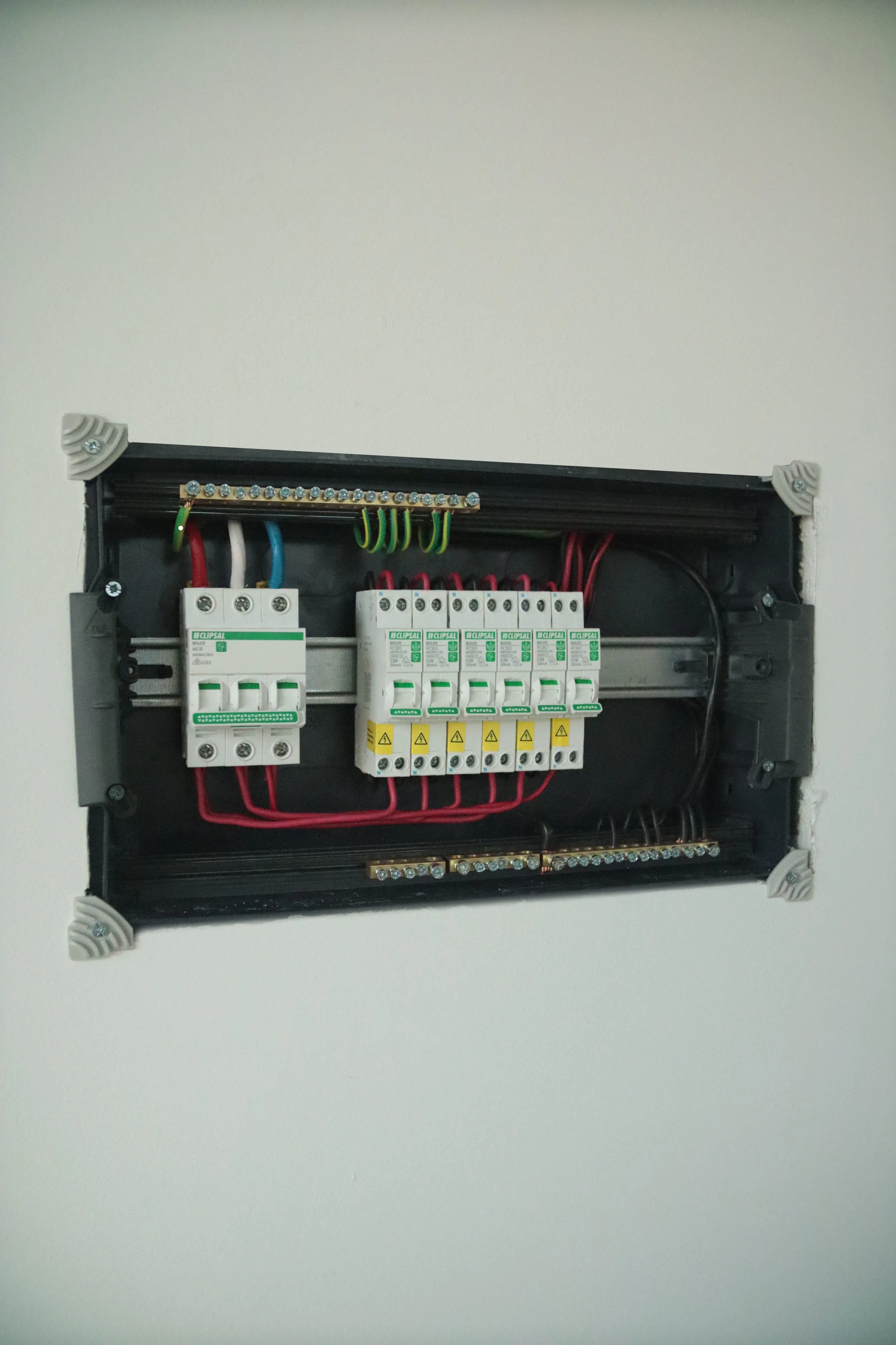 Electrical breaker panel with switches and wiring inside a black box on a white wall.