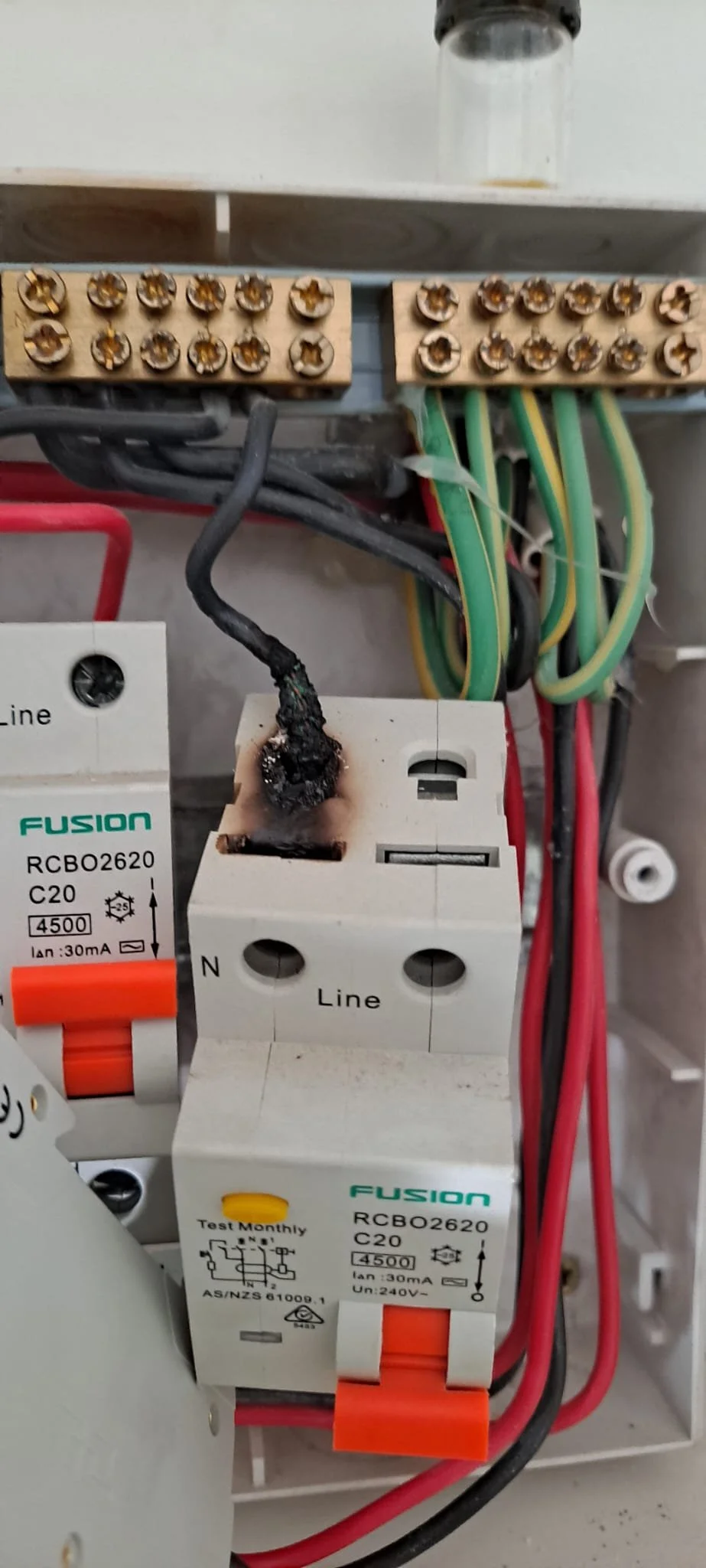 Electrical wiring and components, including a burnt wire connected to a circuit breaker, with various colored wires and terminal connections visible.