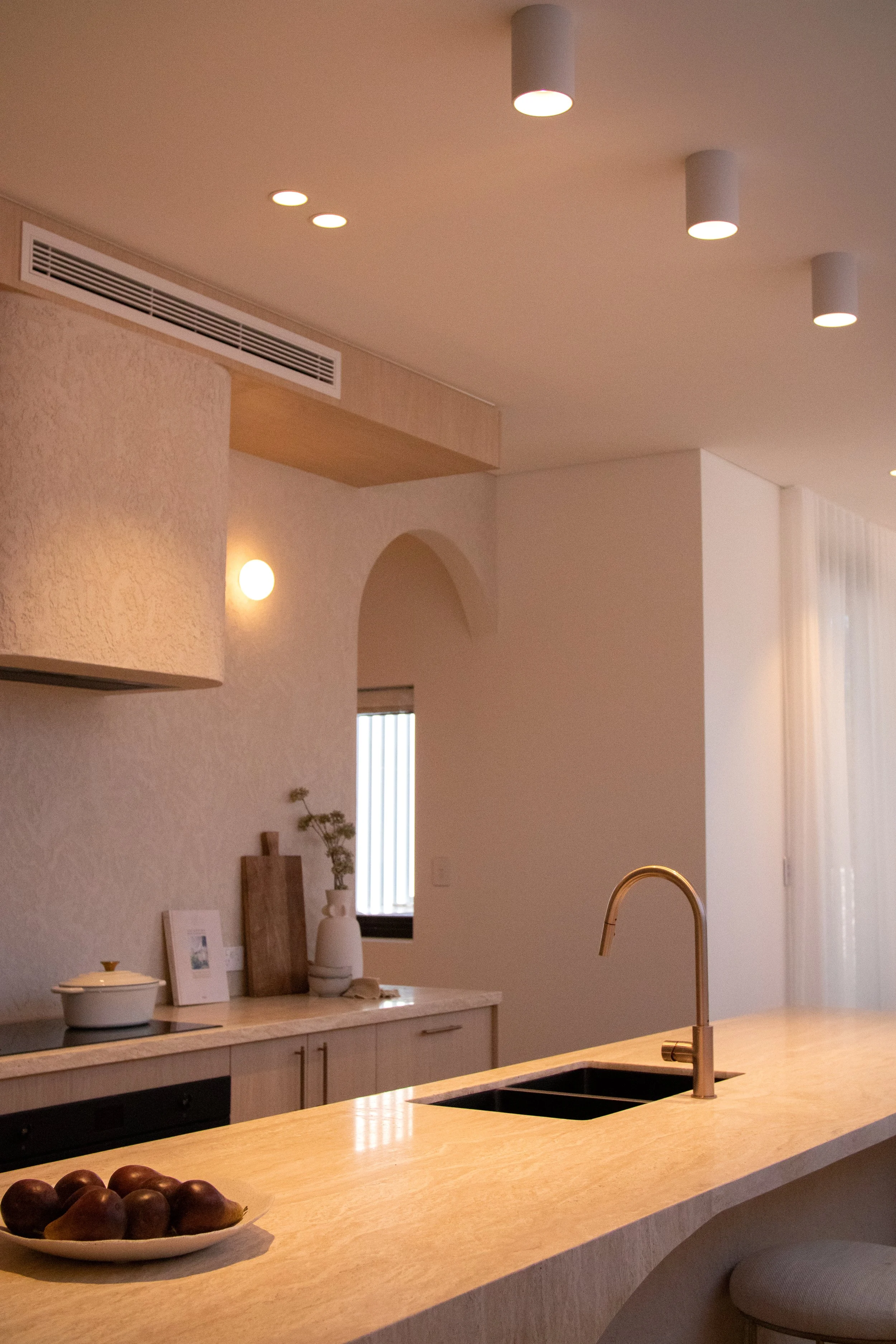 Modern kitchen with wooden countertop, gold faucet, white cabinetry, decorative items, and ceiling lights.