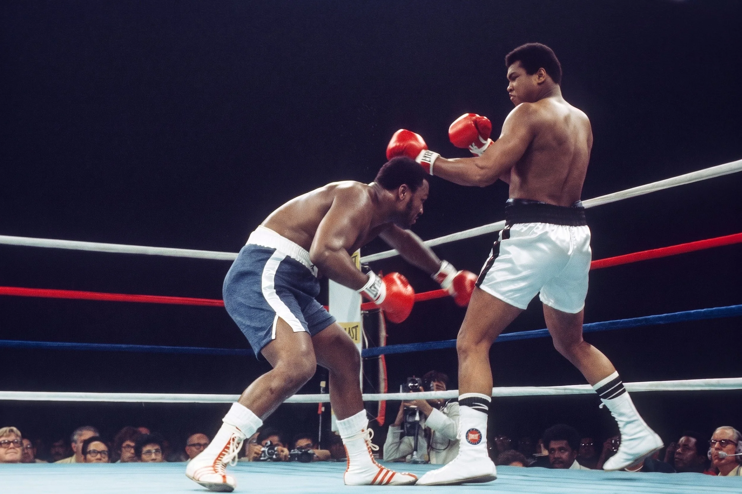 Joe Frazier ducks Muhammad Ali’s left while reaching toward Ali’s body; Don King, Flip Wilson, and broadcaster Don Dunphy are visible at ringside during Ali-Frazier III.