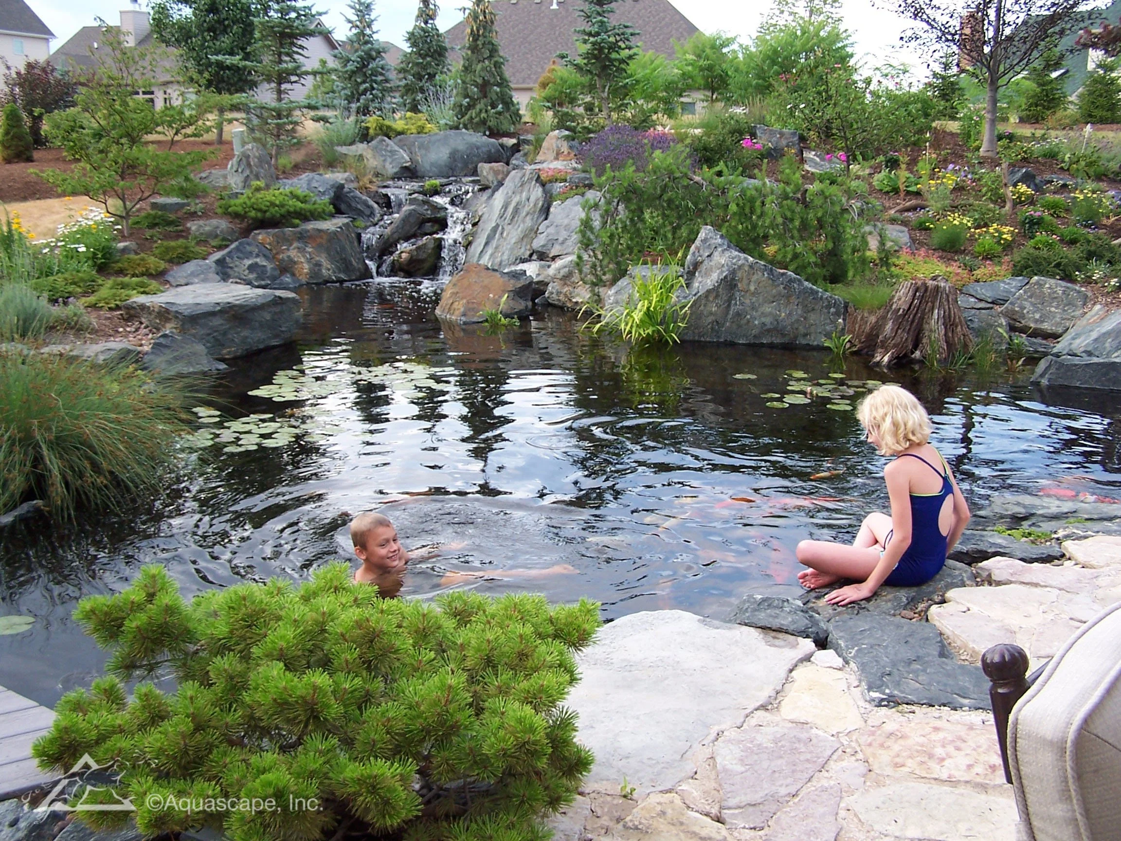 Natural recreational pond with swimming area, waterfalls, boulders, and aquatic landscaping designed for family enjoyment and outdoor recreation.