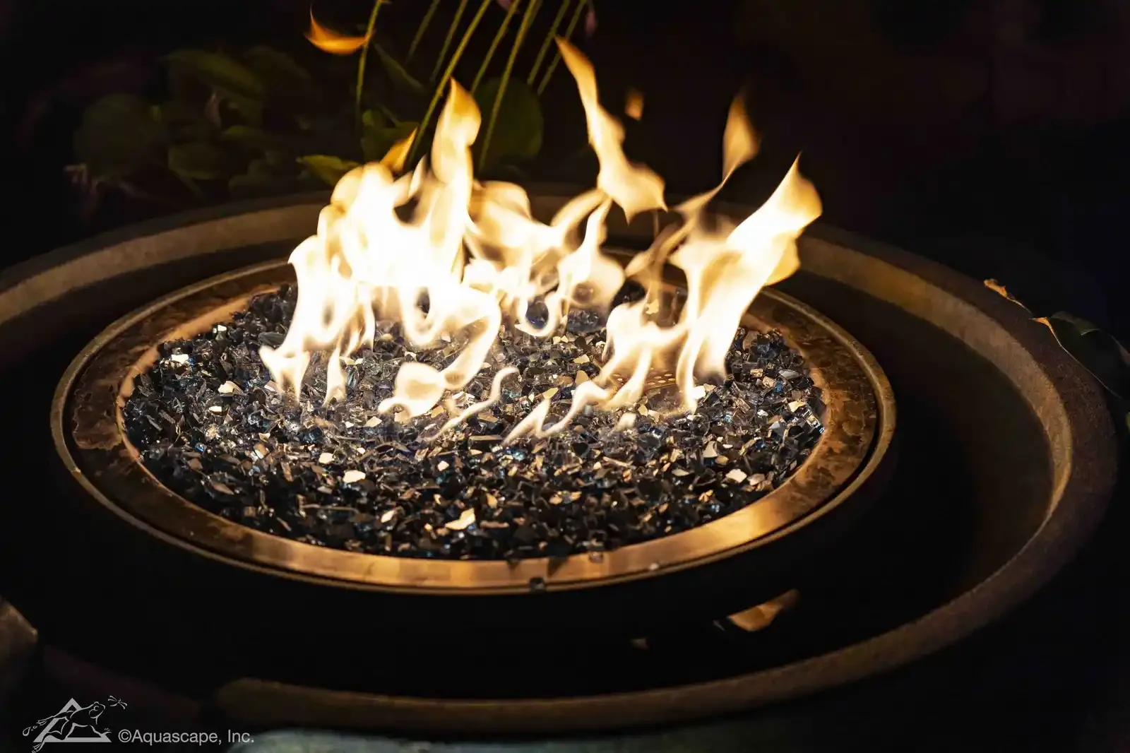 A fire pit with flames burning over black gravel or small stones inside a metal ring.