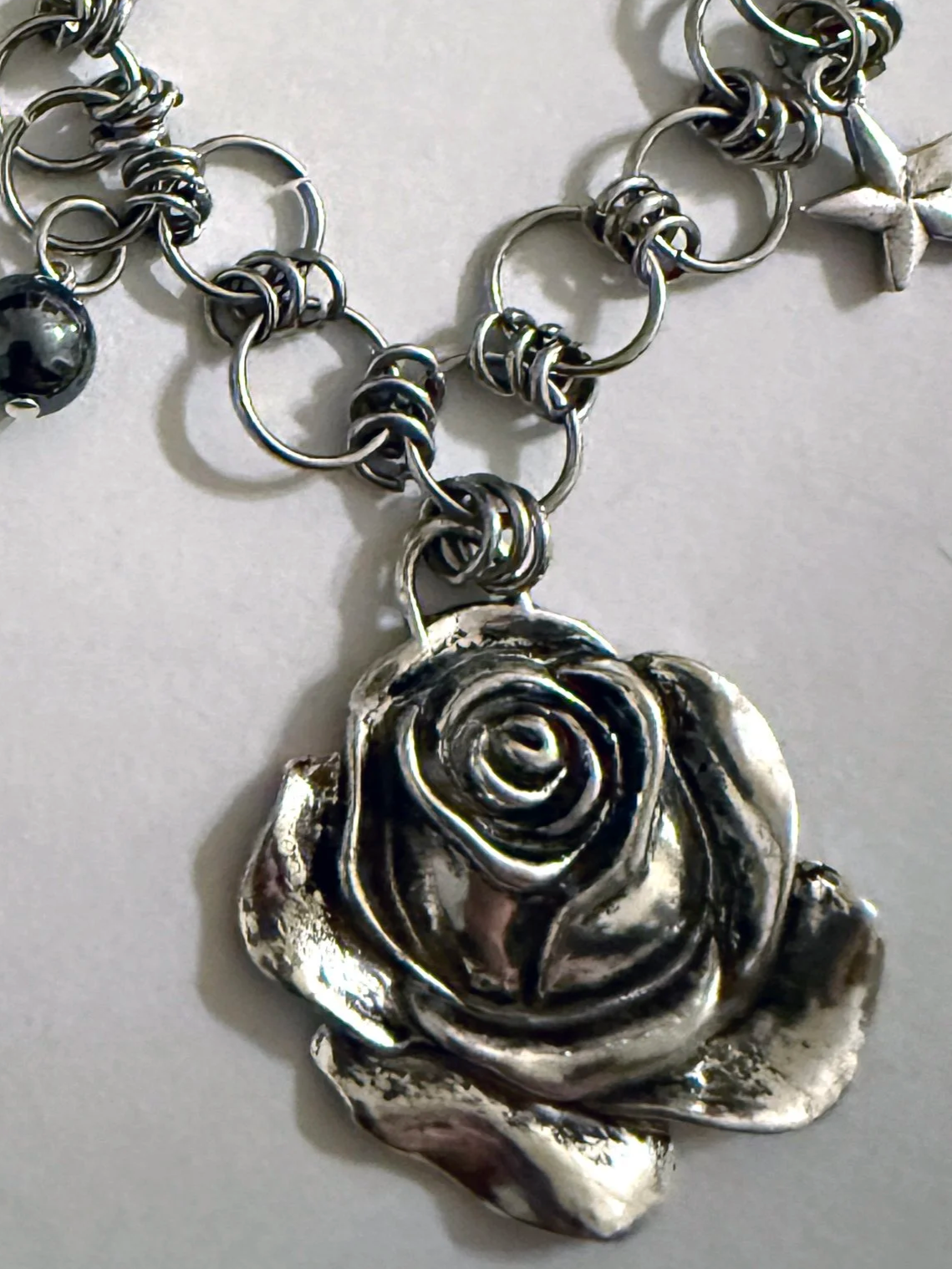 close up image of a silver rose pendant on a chain necklace