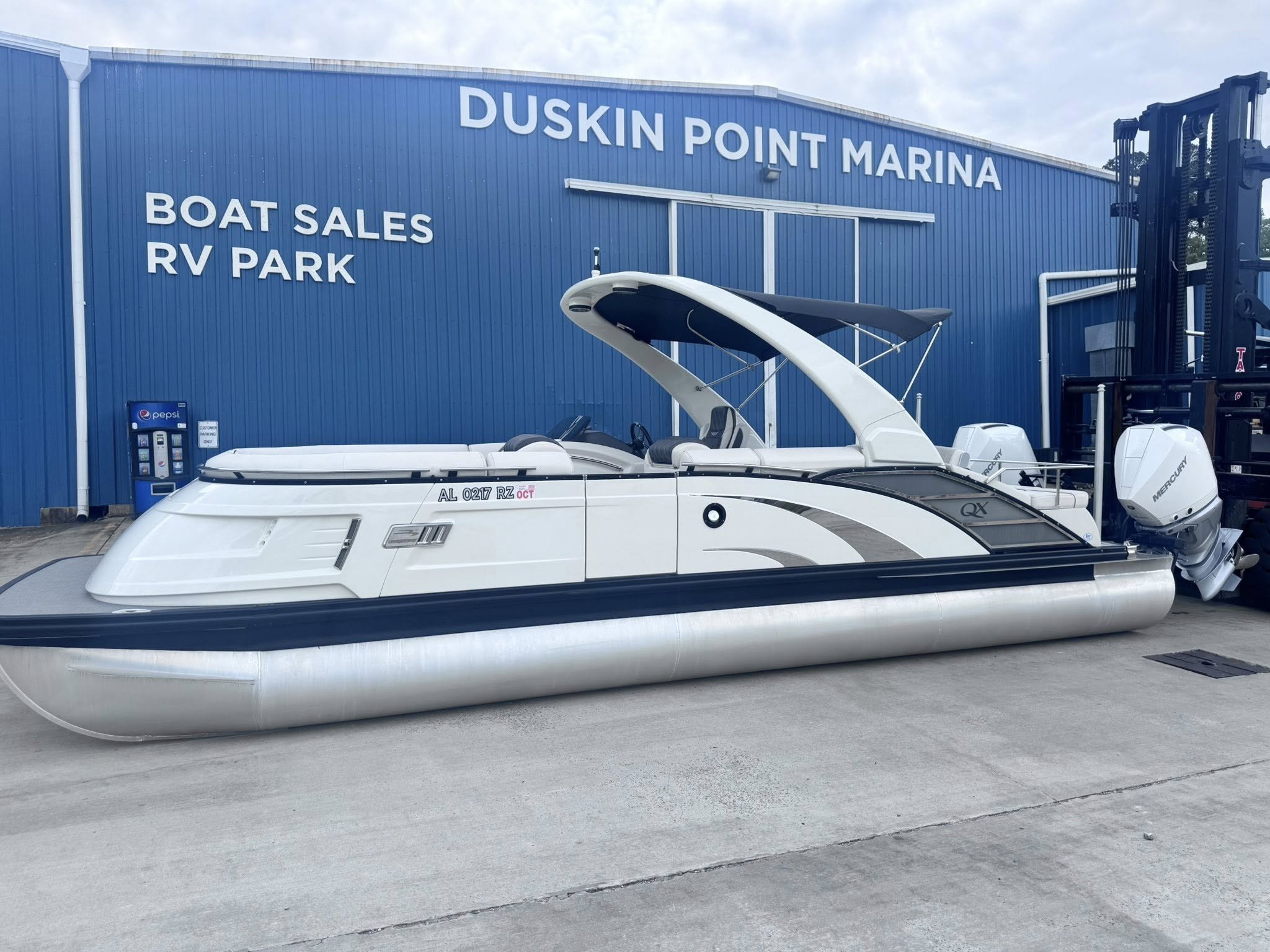 Blue building with large white lettering advertising boat sales, RV park, and a marina. A white boat is parked in front, and a BP vending machine is visible to the left.