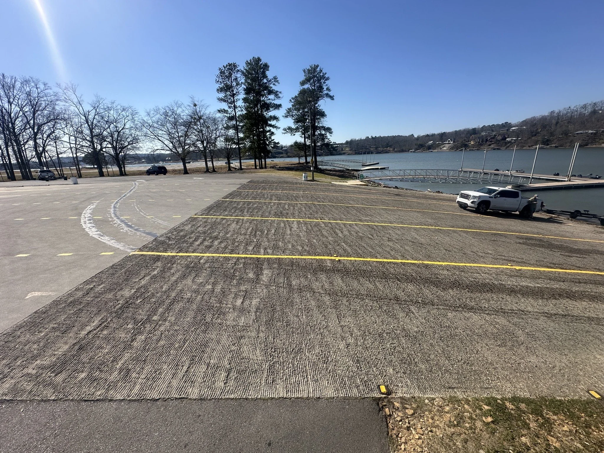 Parking lot and Public Boat launch at Smith Lake Park, near a lake with a small dock, surrounded by trees and hills, under a clear blue sky.
