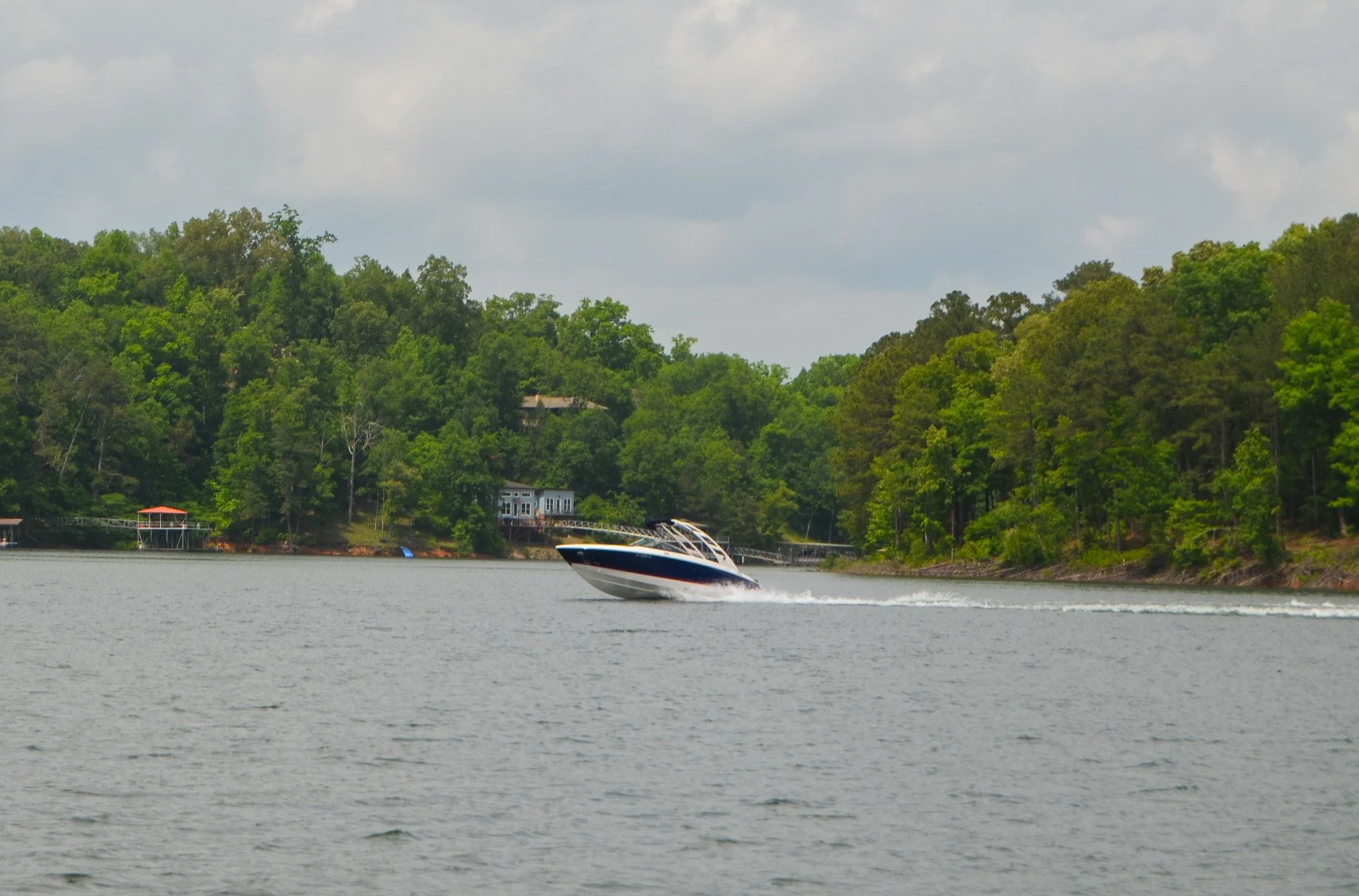 A boat is going across Smith Lake with a lush green forest and house in the background.