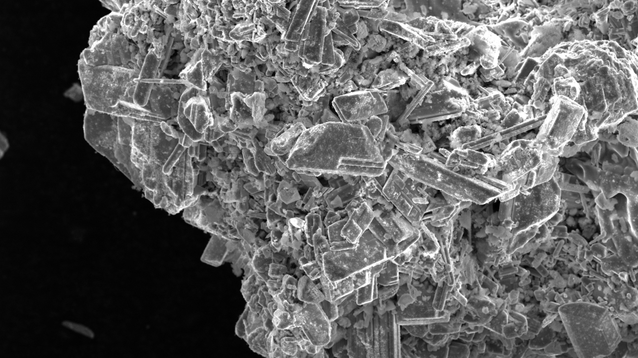 Close-up of crystalline mineral particles, a catalyst, under a microscope, showcasing jagged, uneven textures.