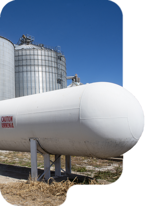 Large white hydrogen storage tank outdoors with industrial silos in the background against a clear blue sky.