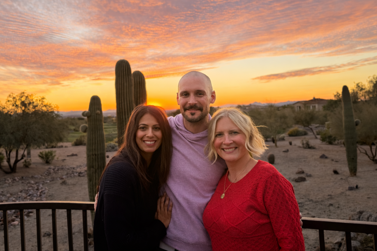 Three smiling adults standing outdoors during sunset in a desert landscape with cacti and rolling hills.