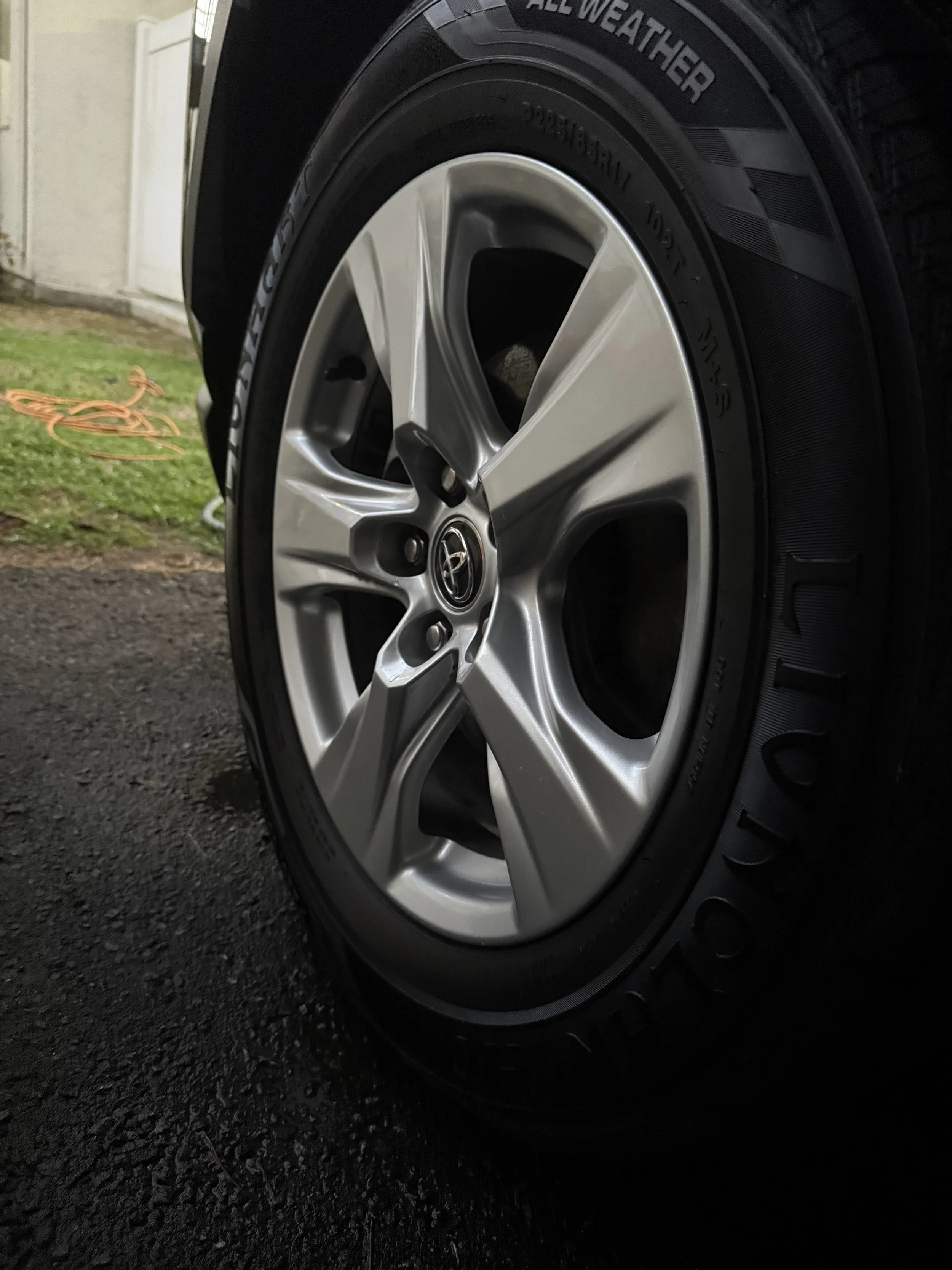 Close-up of a car tire and alloy wheel on a black vehicle, with the Toyota logo at the center of the wheel, parked on an asphalt surface.