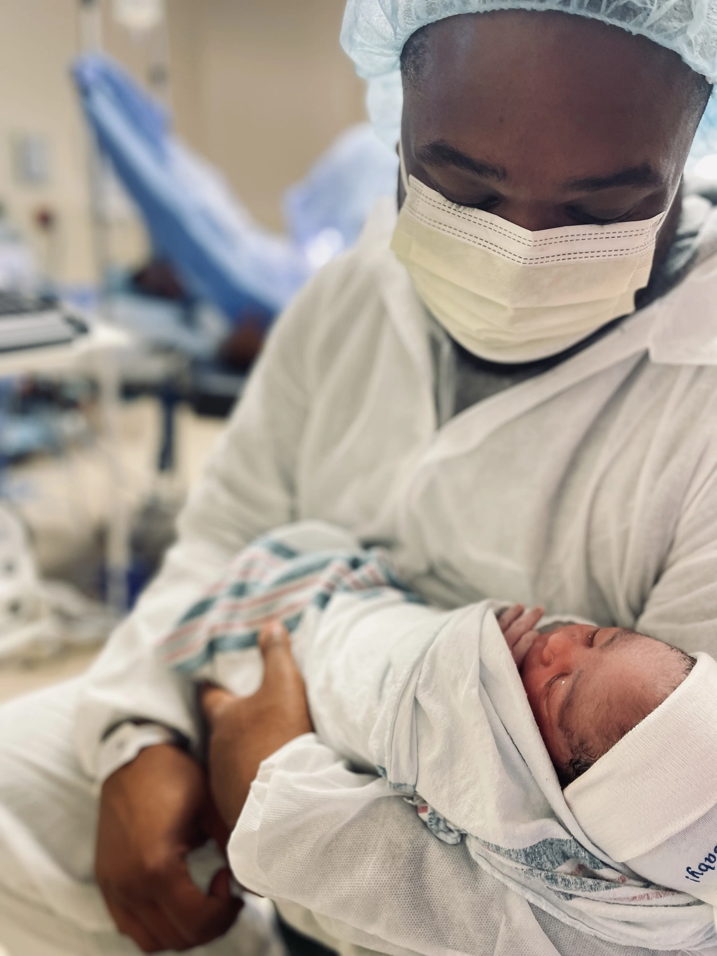 A healthcare worker in protective gear holding a newborn baby in a hospital setting.