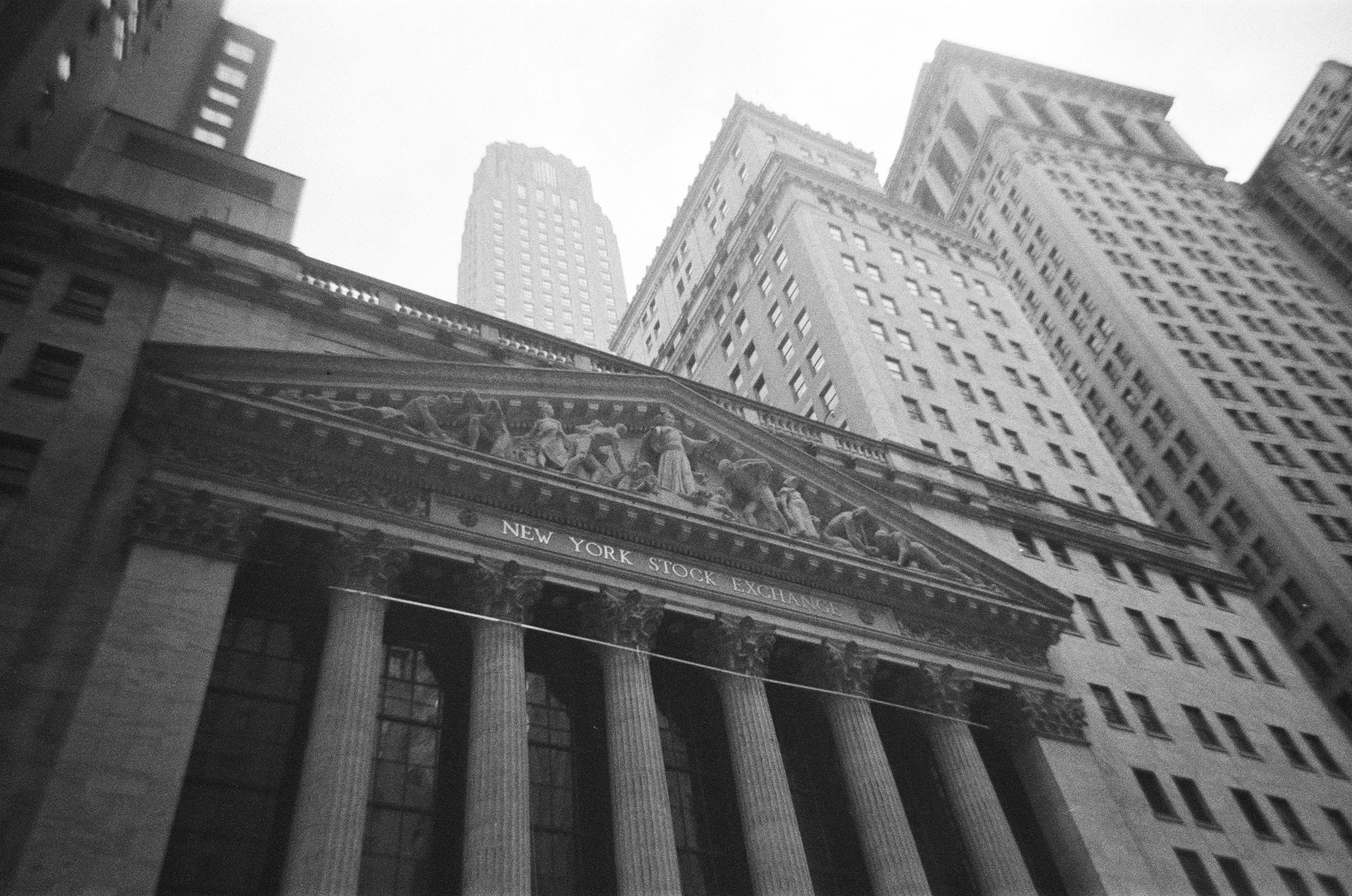 Representing Ananta Strategic's for-profit customers, a black and white photo of the New York Stock Exchange building with tall skyscrapers in the background, viewed from below.