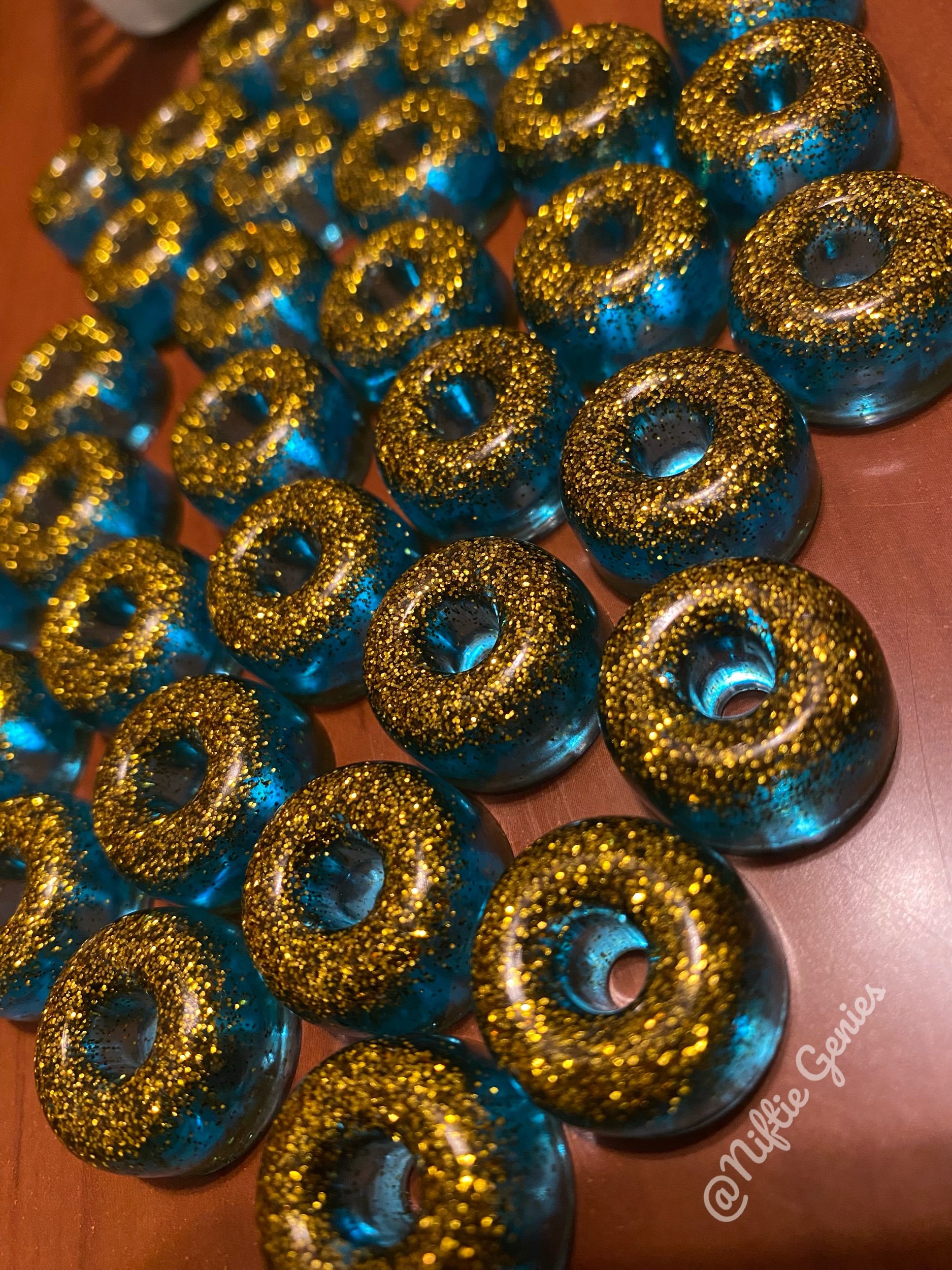 Blue donut-shaped resin charms with gold glitter on top, arranged on a wooden surface.