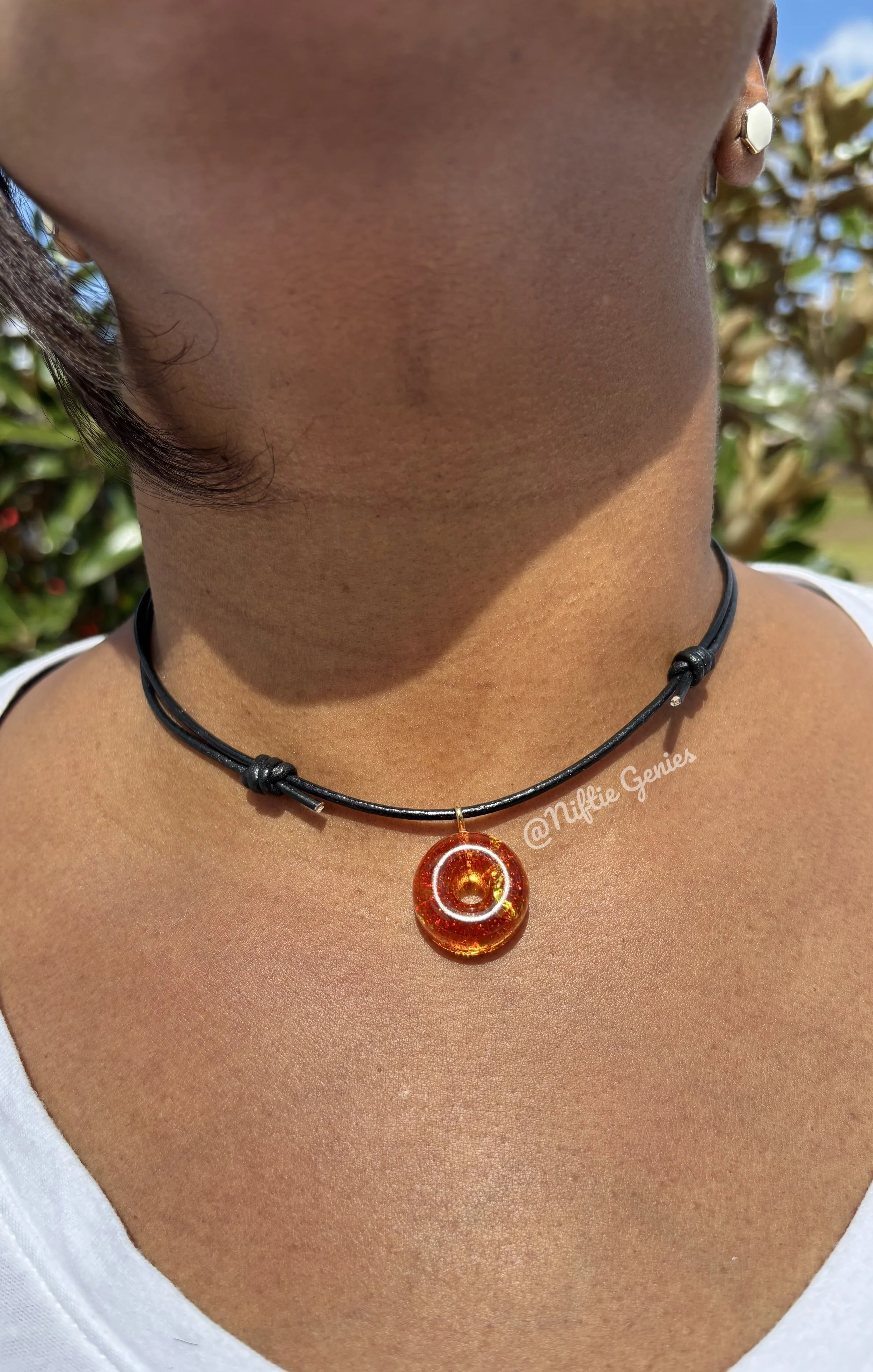 Close-up of a person’s neck wearing a black cord necklace with an amber-colored circular pendant and a small gold earring.