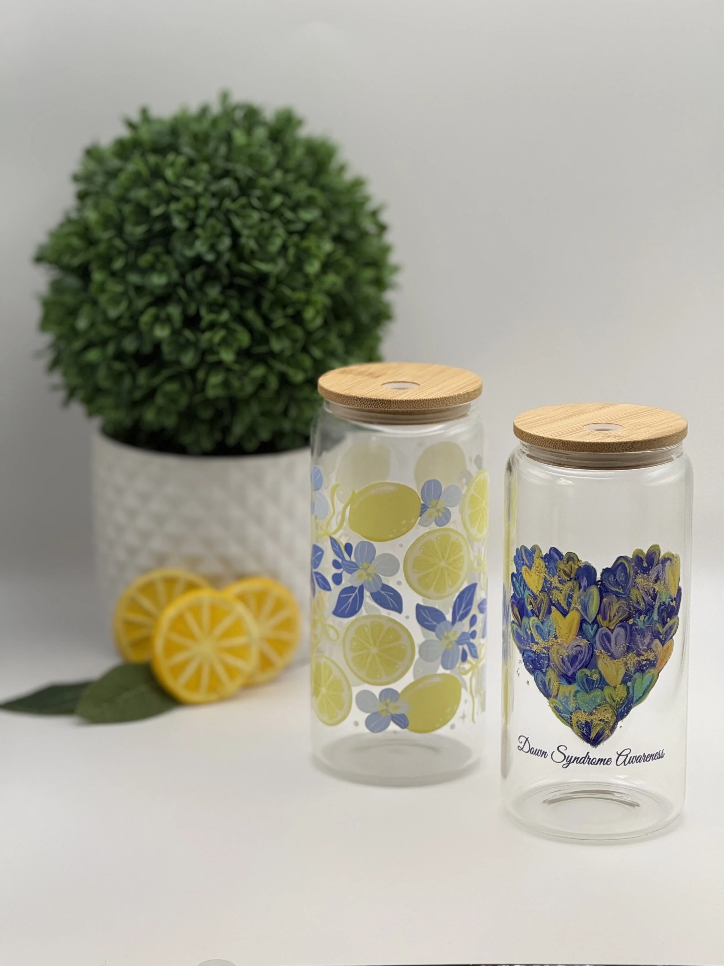 Decorative glass jars with lemon and flower patterns, with a potted green plant and lemon slices with leaves in the background.