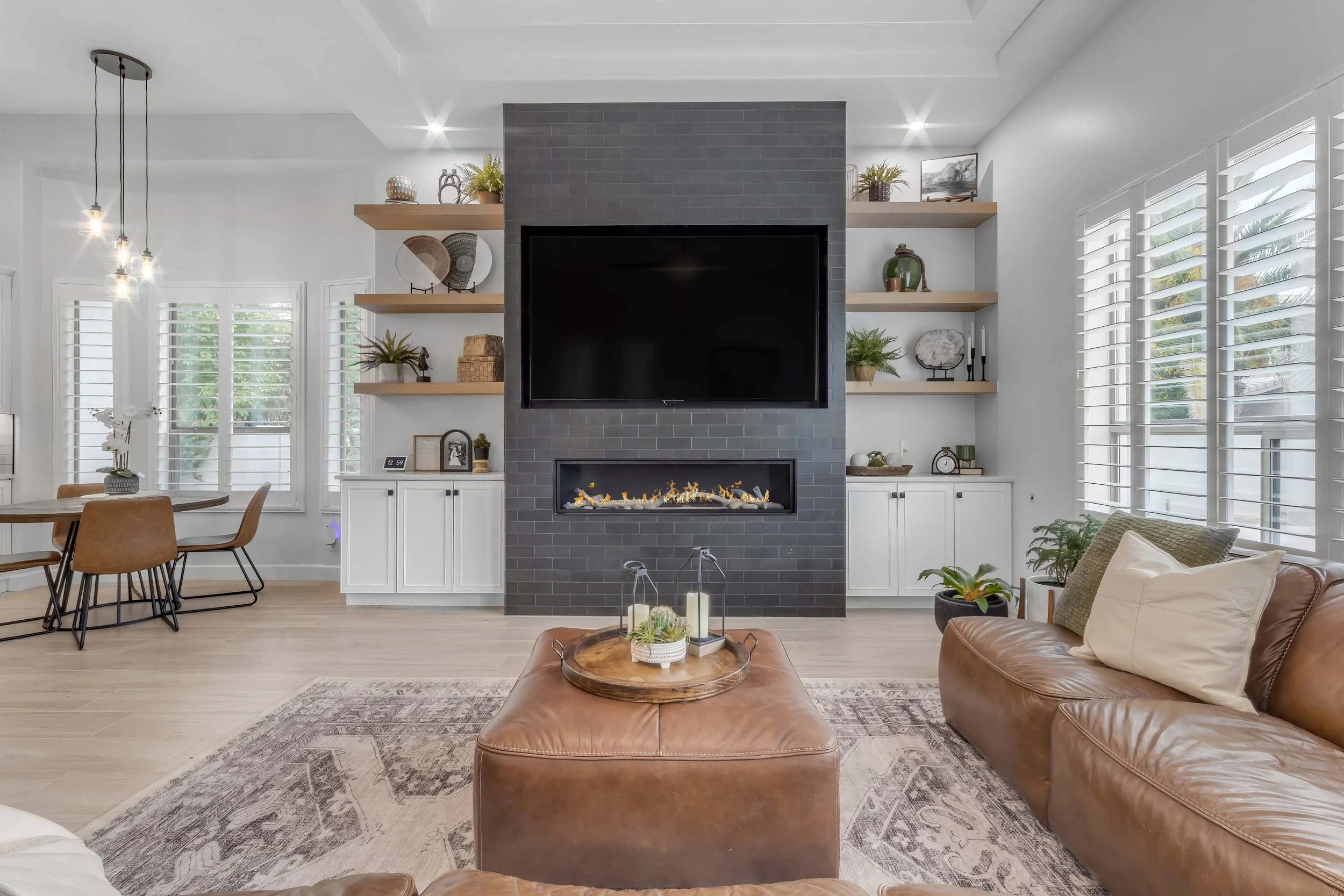Living room with fireplace, wall-mounted TV, brown leather sofa, and wooden open shelves with decorative items.
