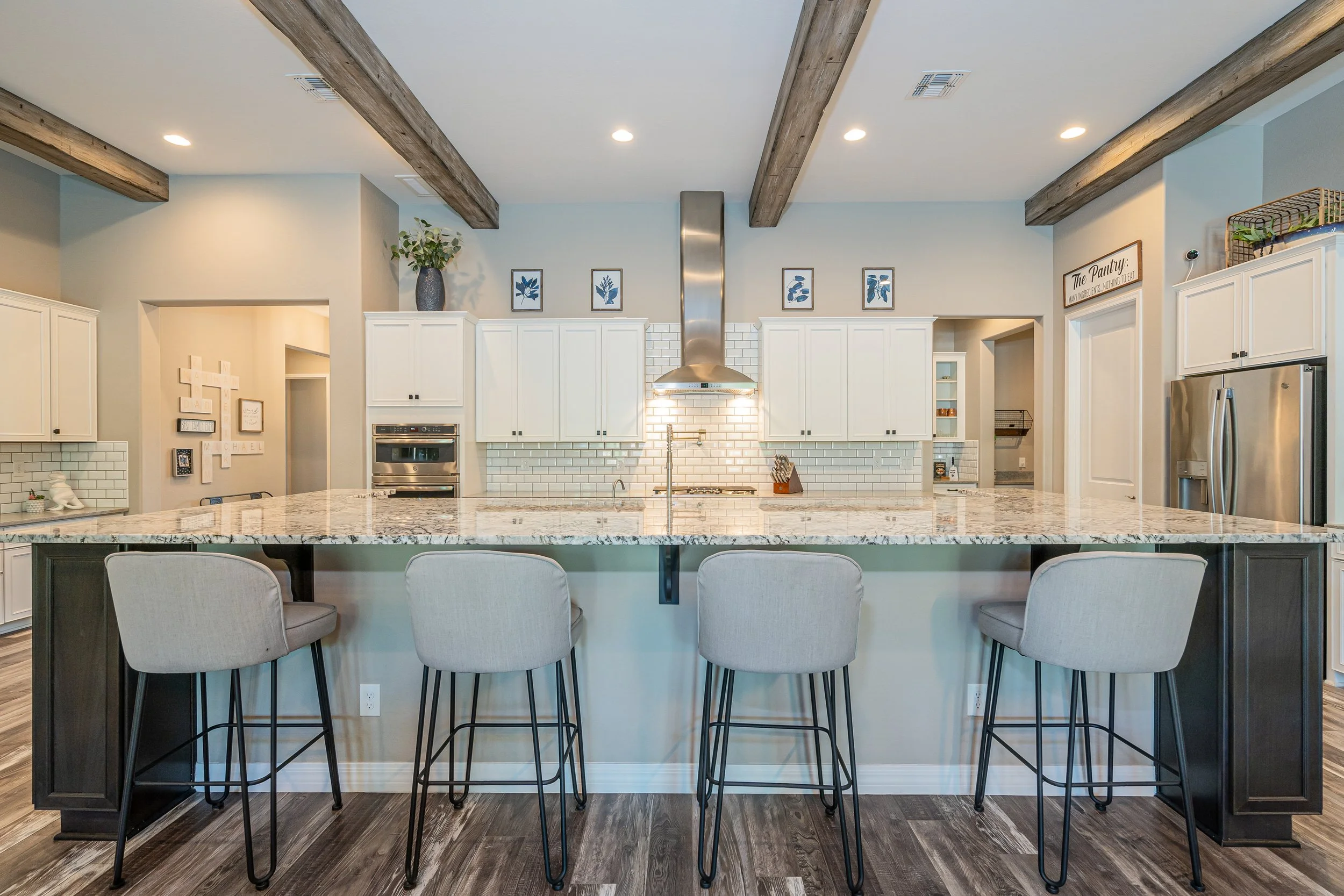 Modern kitchen with white cabinetry, granite island, stainless steel appliances, and four barstools with beige cushions.