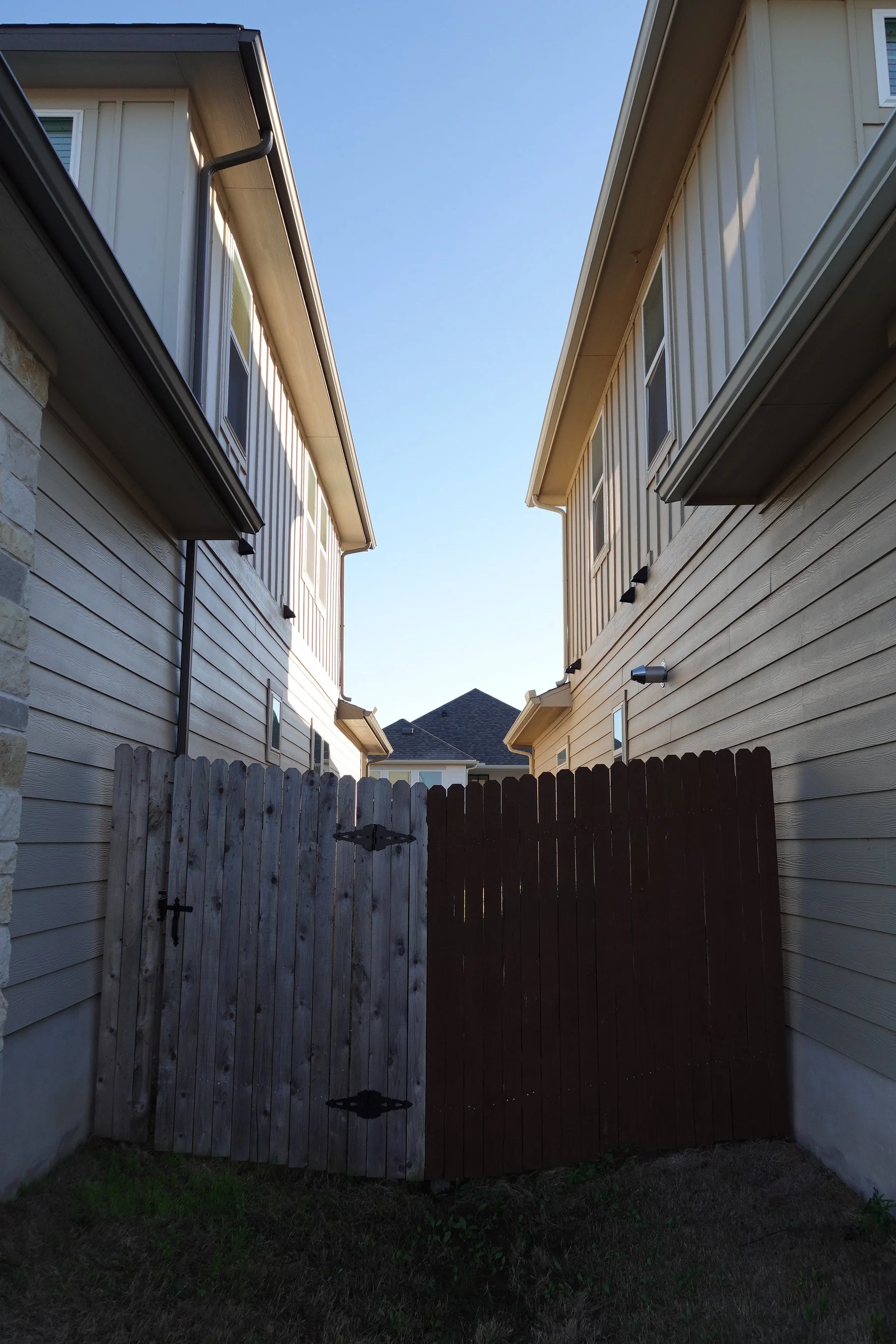 Before and after fence staining by Golden Hour Painters in Buda, showing a gray weathered fence transformed with a warm brown stain.