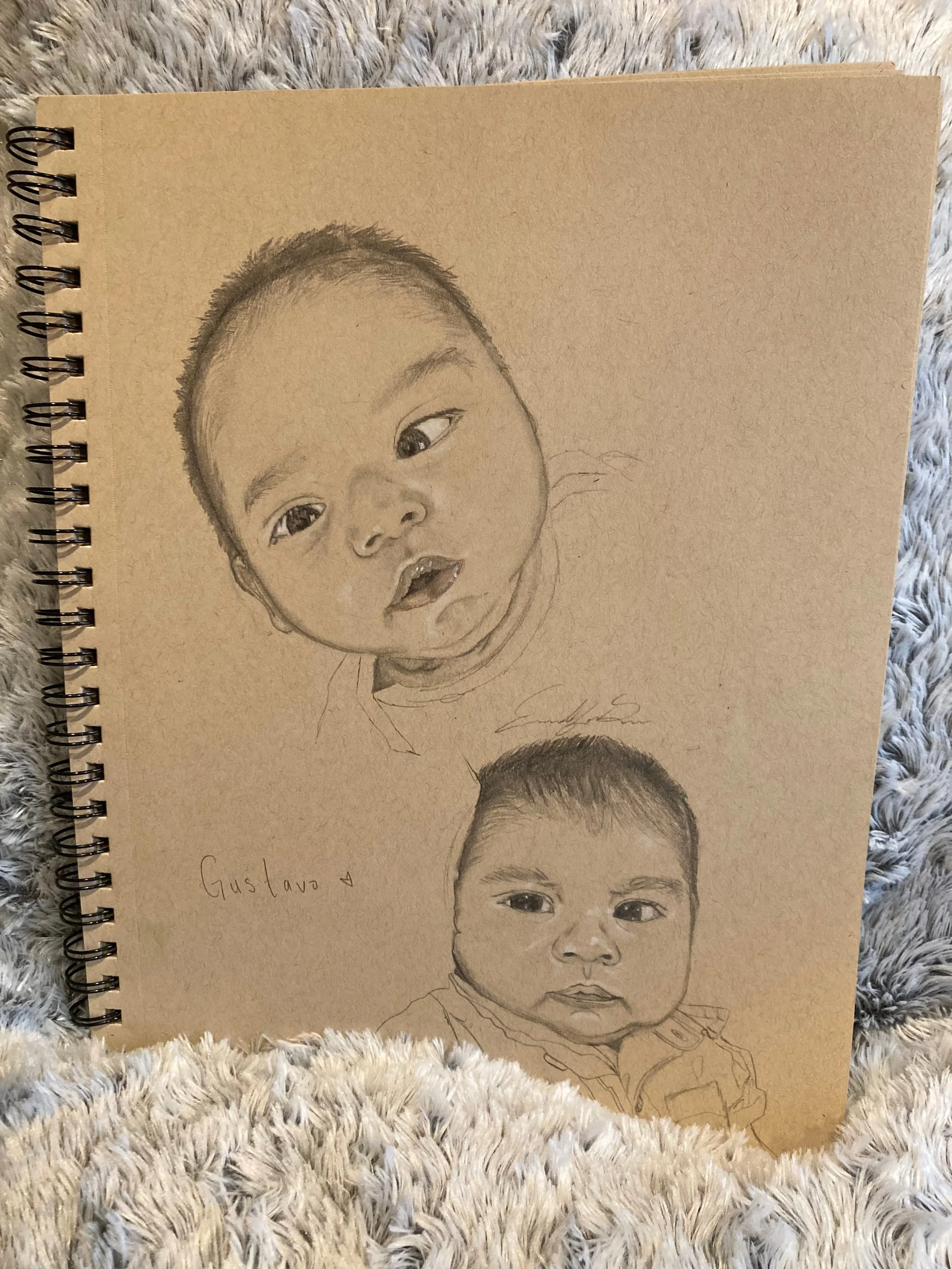 Sketch of a child's face on beige paper with handwritten name 'Gustavo' and a signature below, placed on a soft, furry surface.