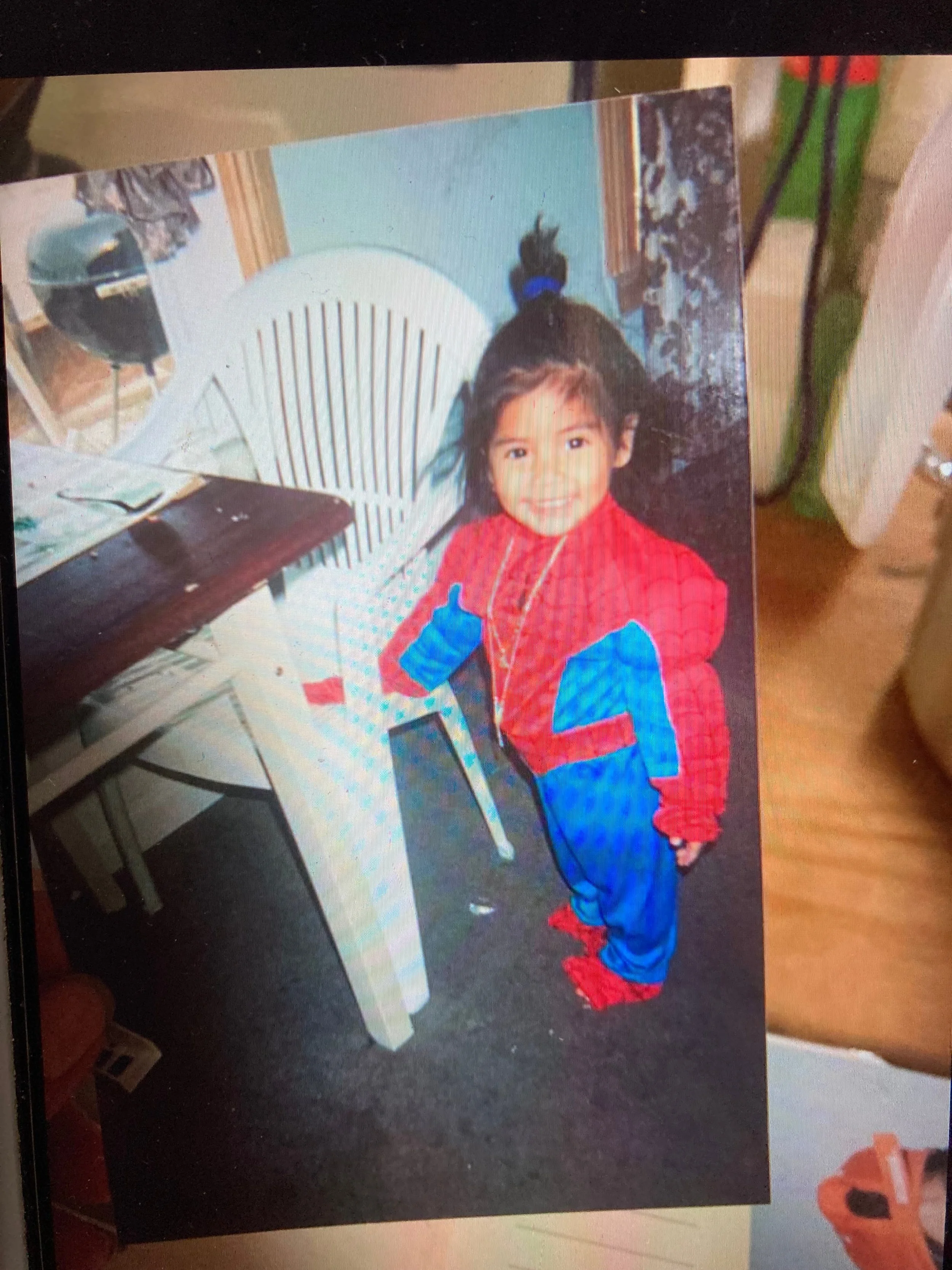 Young child dressed as Spider-Man smiling in a room, standing near a table.