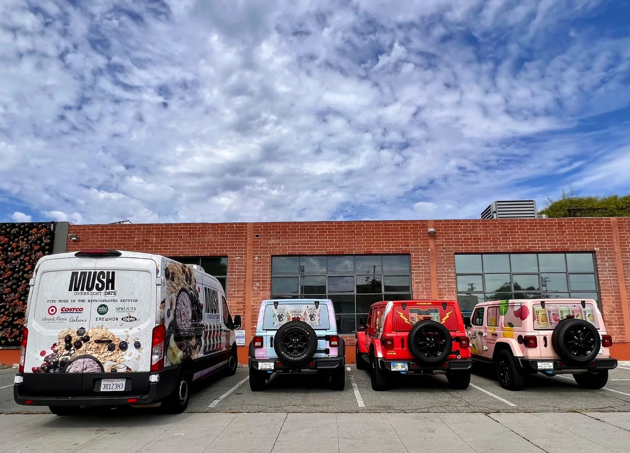 Four decorated vans parked in front of a brick building under a partly cloudy sky.