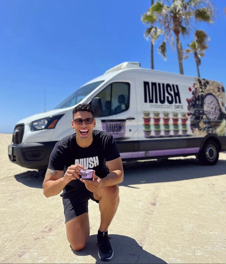 Ambassador kneeling on the beach in front of a MUSH-branded van