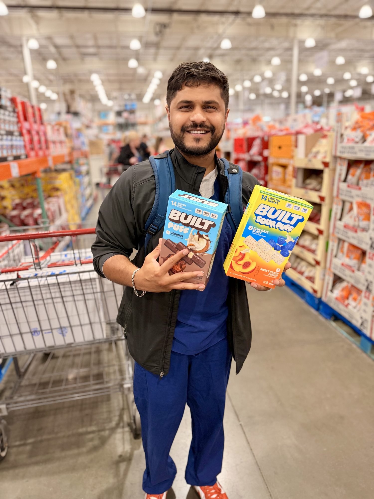 Costco member in scrubs holding two boxes of BUILT Puff in the warehouse aisle