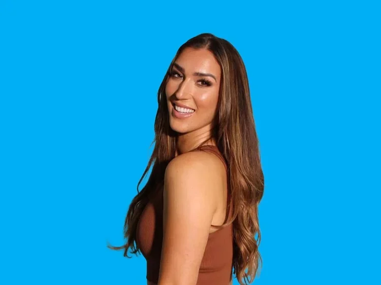 A woman with long brown hair smiling and winking at the camera against a bright blue background.