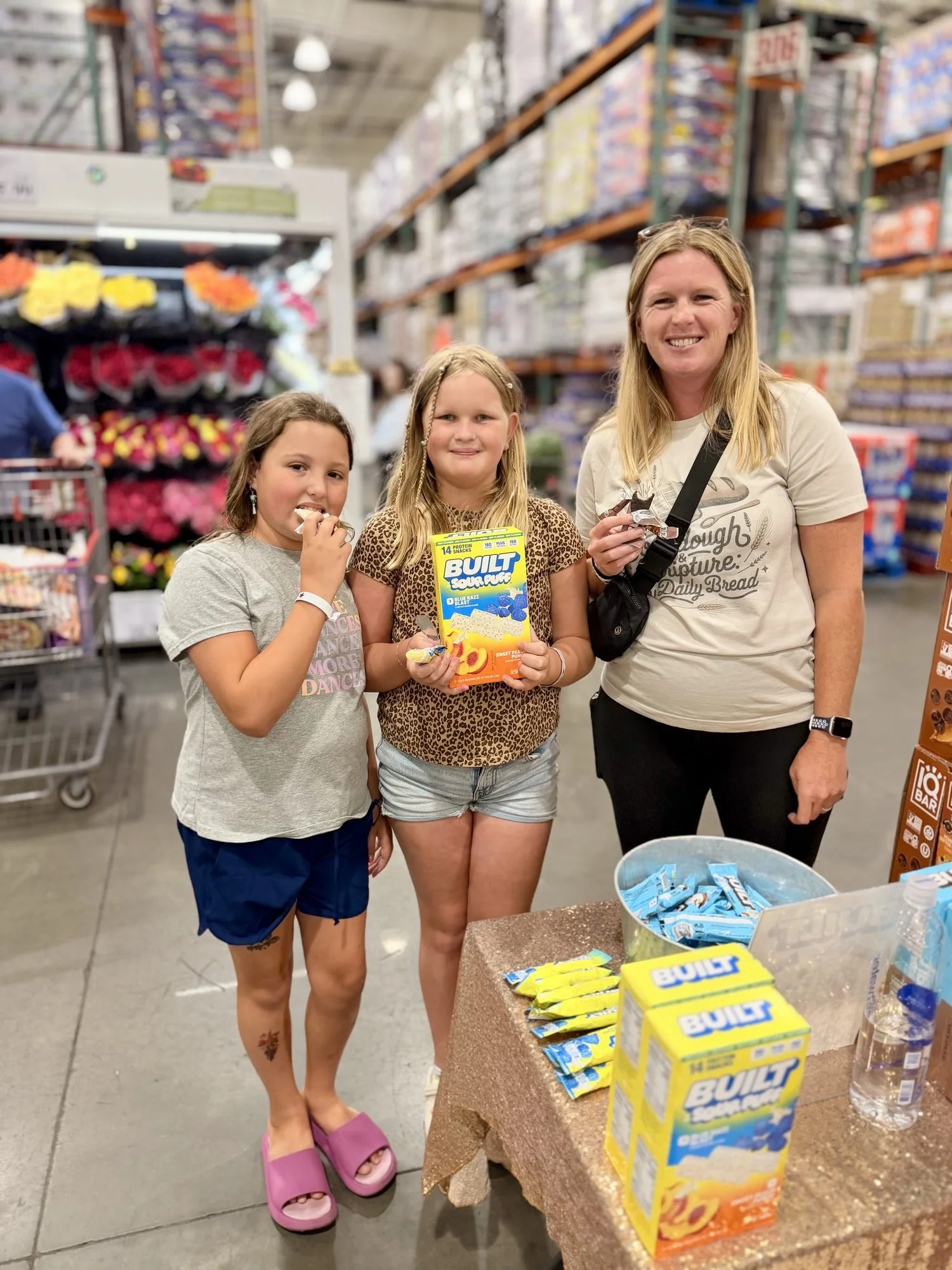 Two girls and their mom holding BUILT Sour Puffs at a Costco roadshow sampling table