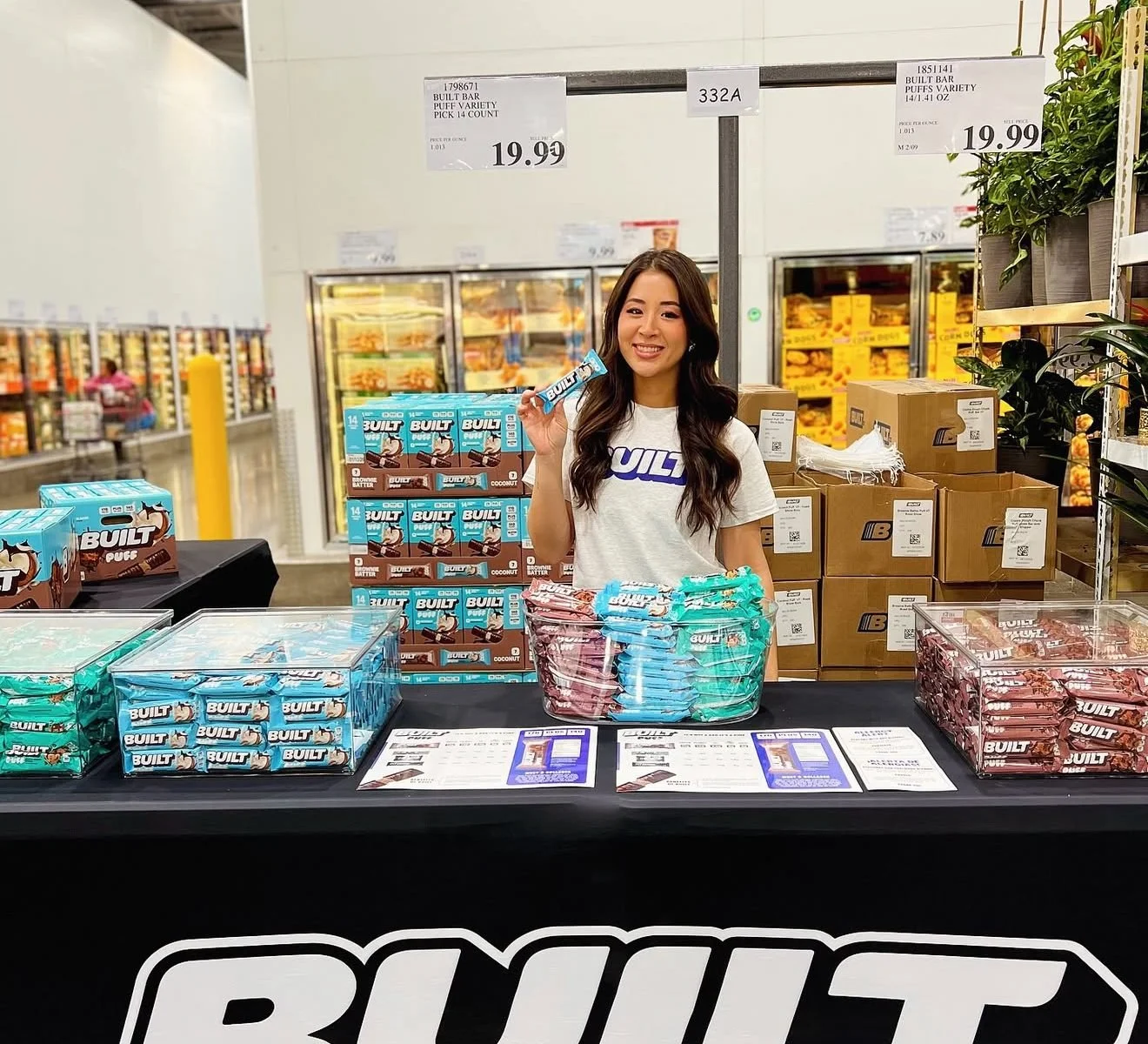 Brand ambassador at a BUILT-branded Costco roadshow sampling table with BUILT Puff boxes and price signs