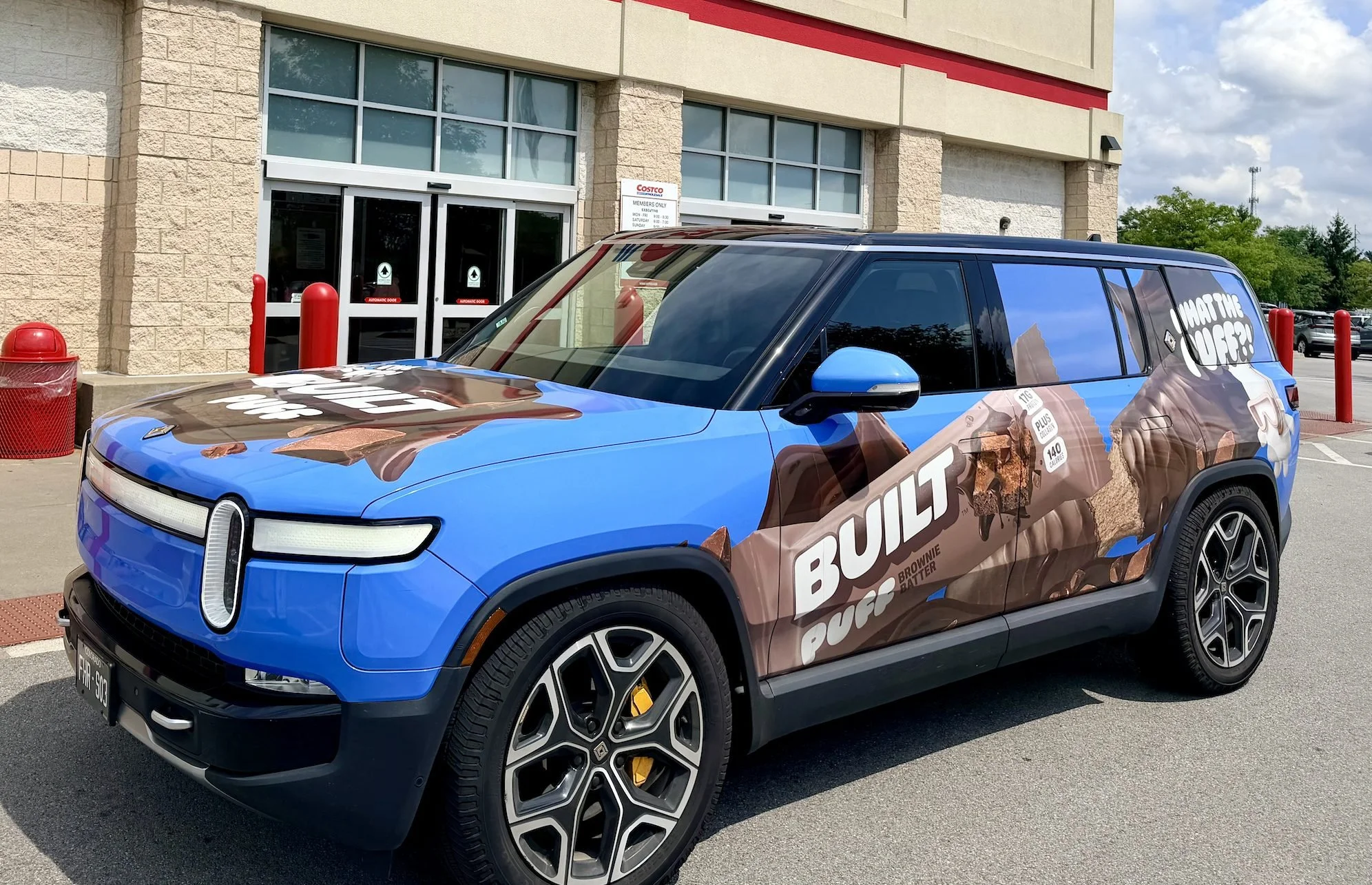 Blue and brown BUILT Puff-wrapped Rivian SUV parked at a Costco Wholesale warehouse entrance