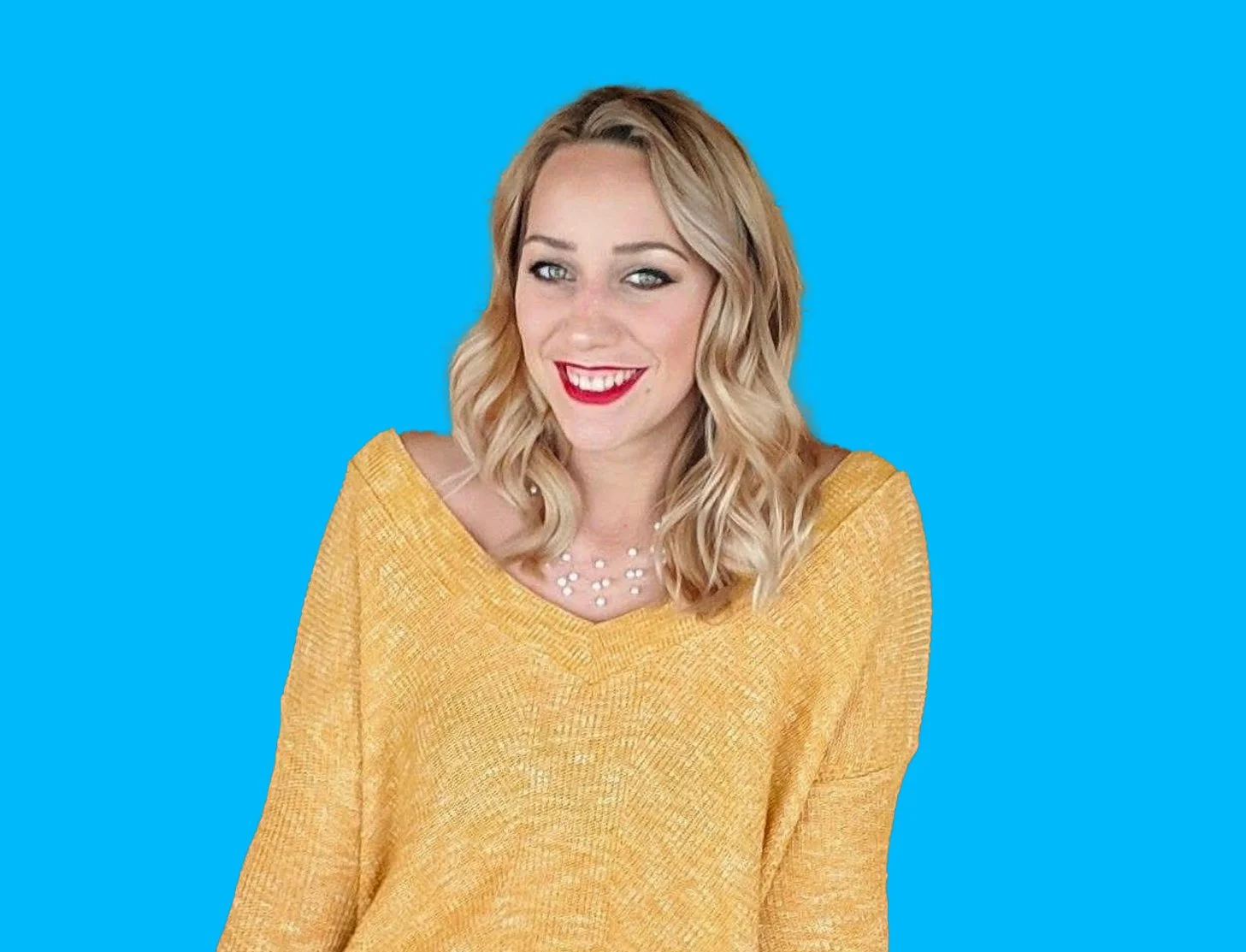 A woman with wavy blonde hair, red lipstick, and a yellow sweater smiling and looking to the side against a bright blue background.