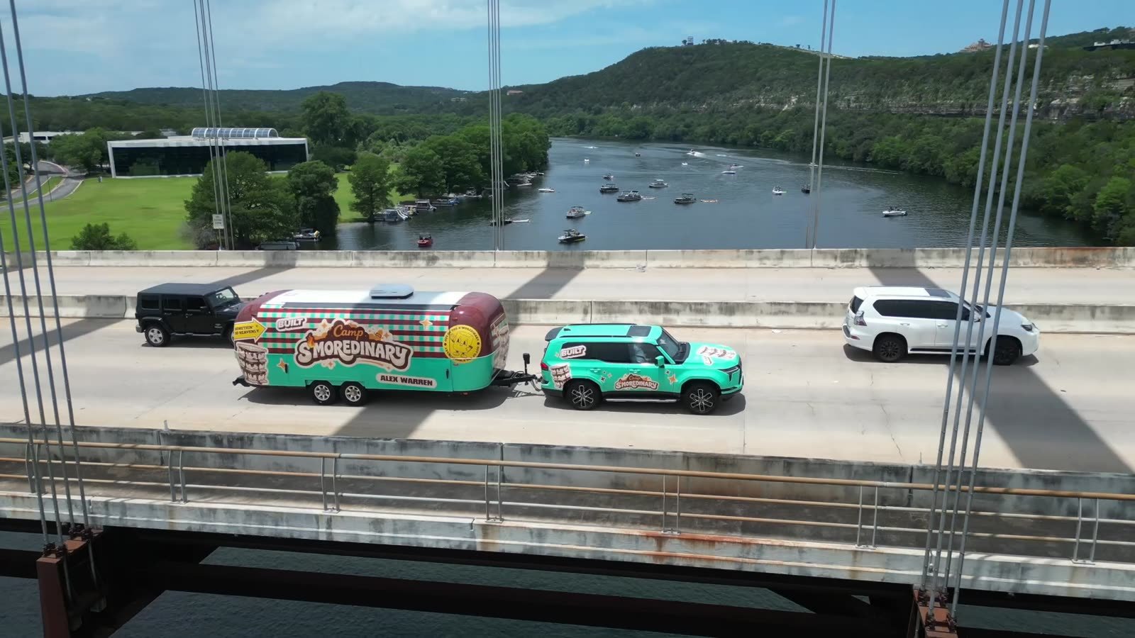 Teal SUV towing the Built x Alex Warren Camp S&rsquo;moredinary Airstream across a highway bridge over a river