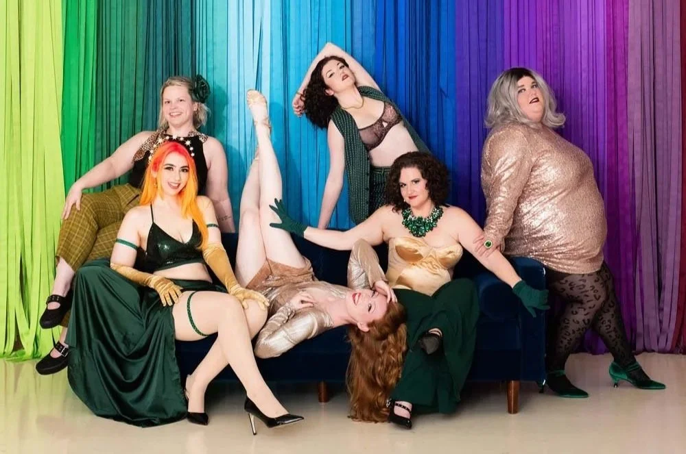Group of six women from Down South Delectables Burlesque Collective posing on a velvet couch in front of colorful curtains