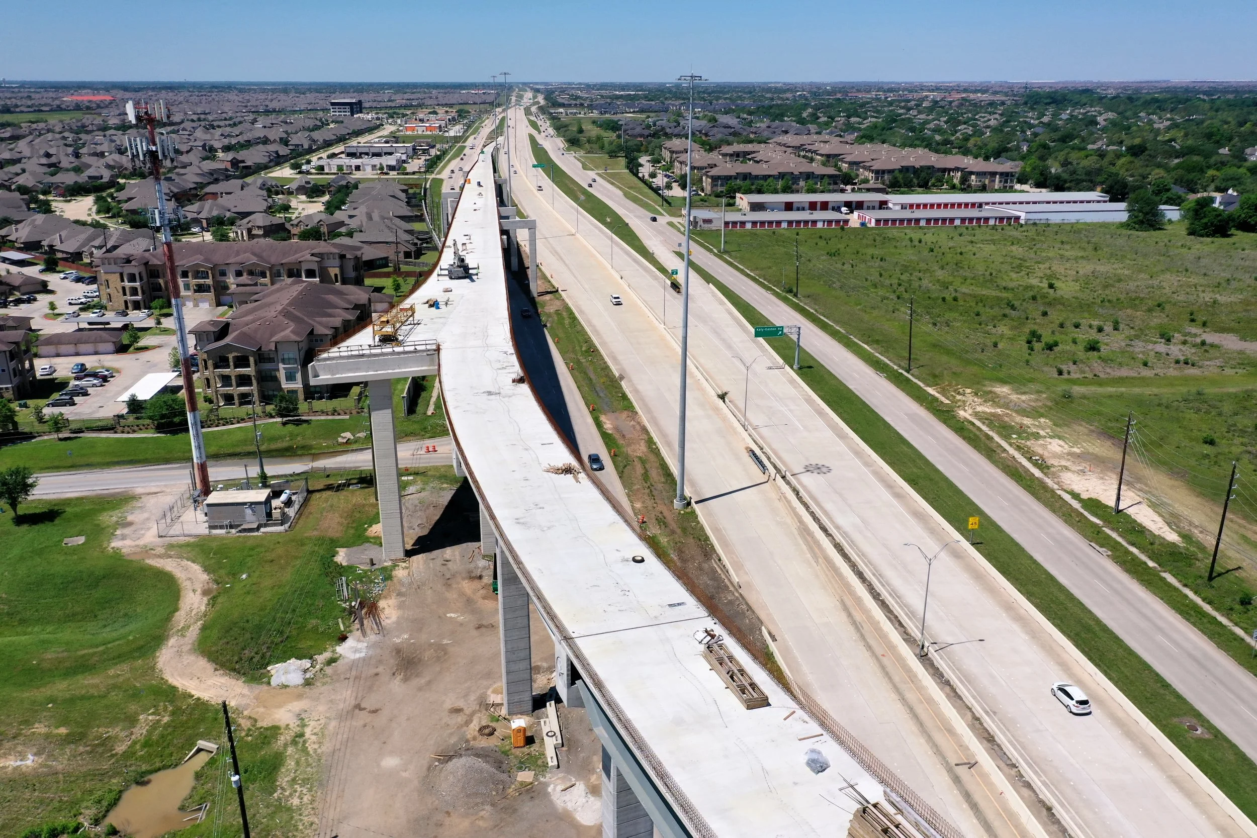 Aerial view of an elevated highway under construction, with residential neighborhoods and open land on either side.
