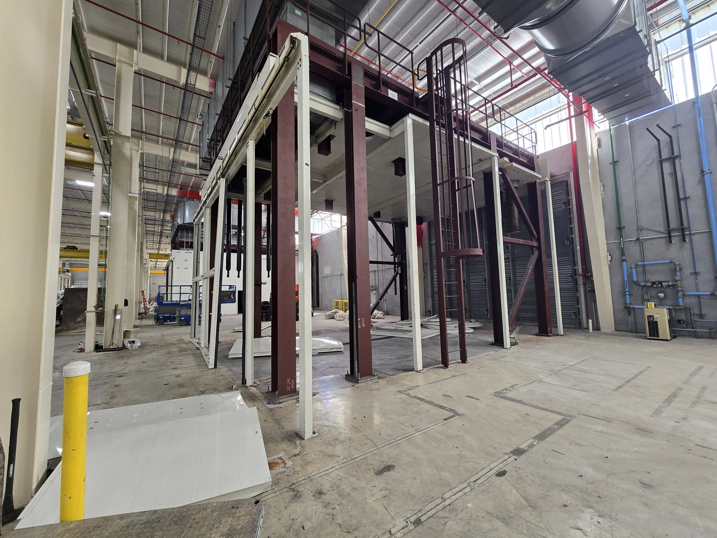 Industrial construction site with metal frame structure and scaffolding in a warehouse or factory setting.