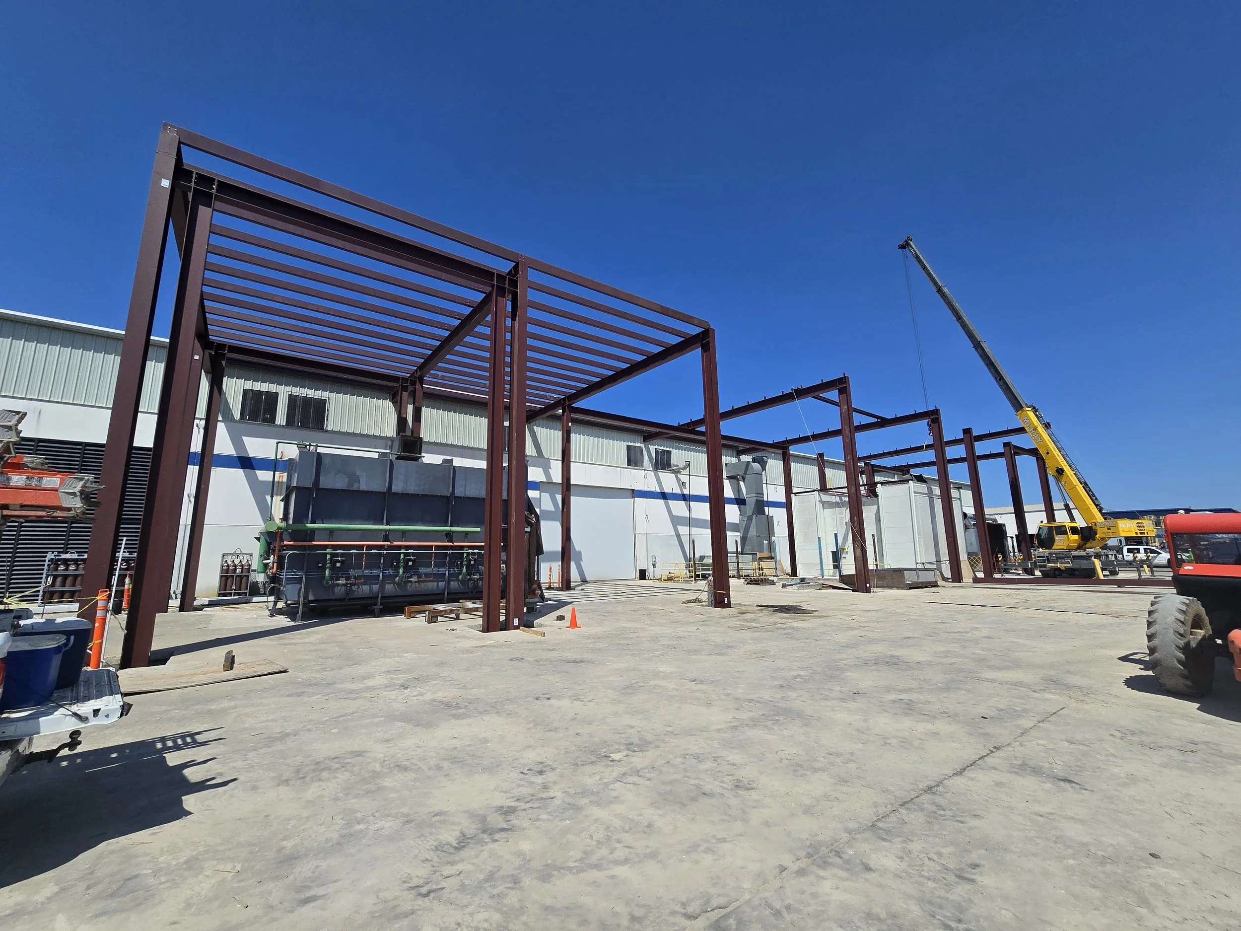 Construction site with steel framing, a yellow crane, and construction equipment on a clear day with a blue sky.