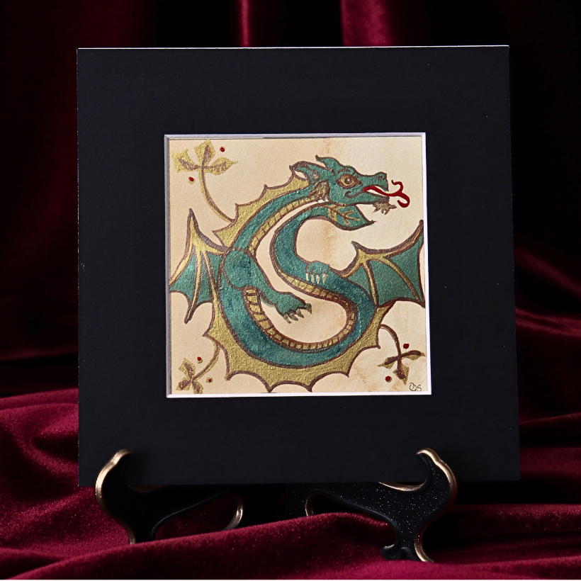 A green and gold dragon forming the initial S, displayed in a black mat on burgundy velvet.