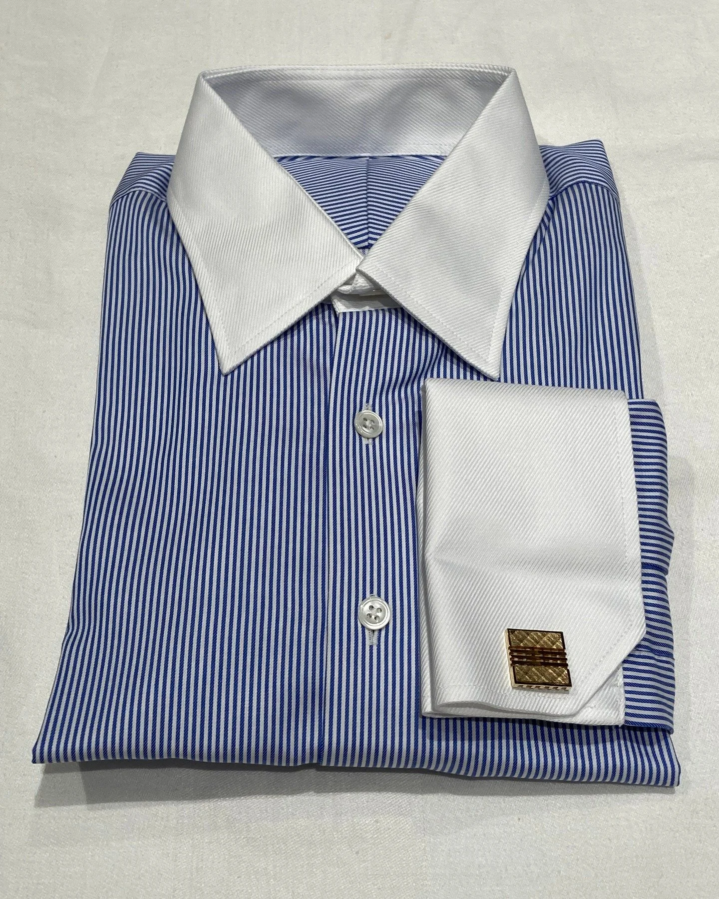 A very elegant striped blue shirt with cut corner French cuffs. While French cuffs are increasingly rare, cut corner French cuffs are especially hard to find. Other differentiating stylistic details include using twill white for the contrast collar a