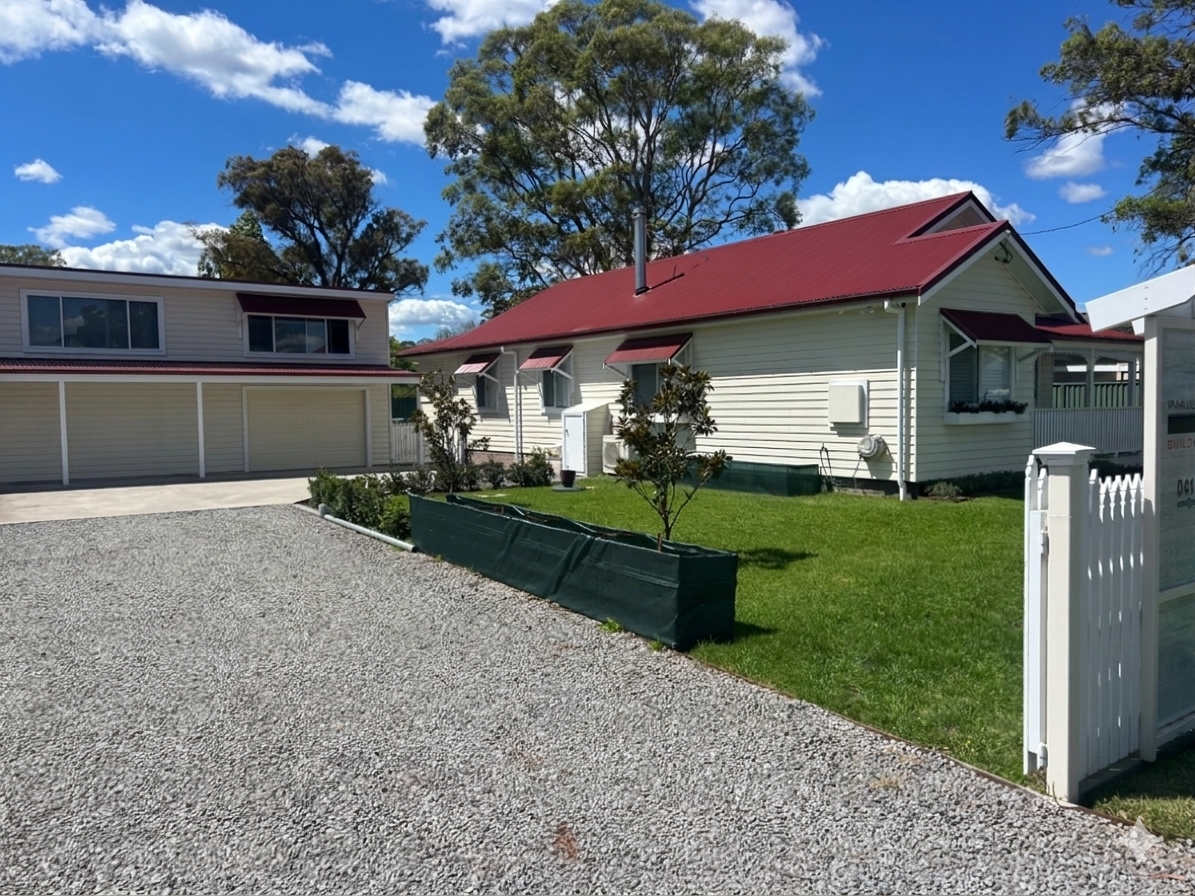 A sunny day scene with a white house with a red roof, a lawn, and trees in the background, along with a neighboring house with a garage.
