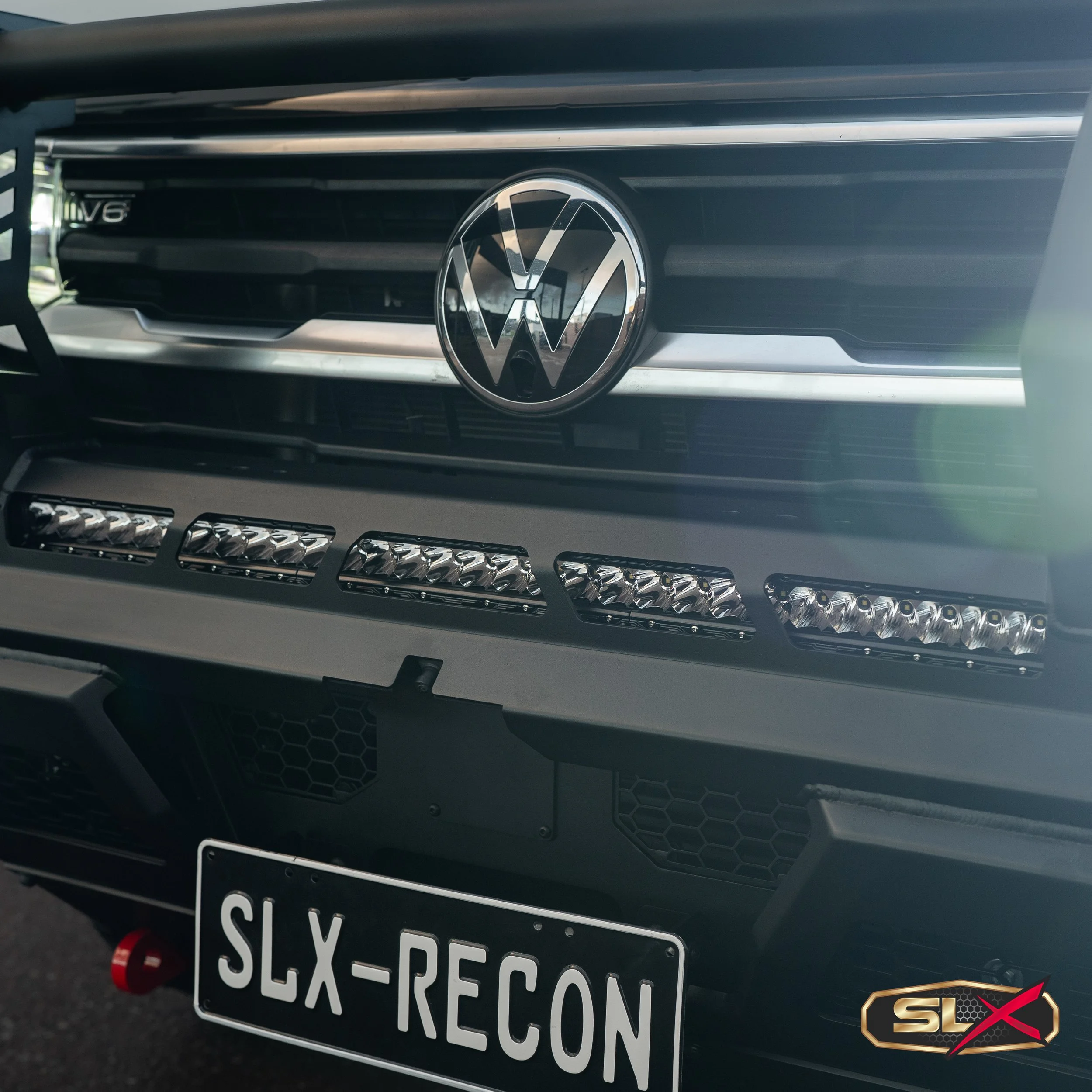 Front view of a Volkswagen vehicle with a German license plate reading 'SLX-REC0N' and LED lights below the grille. The vehicle has a black exterior with a chrome VW emblem on the grille.