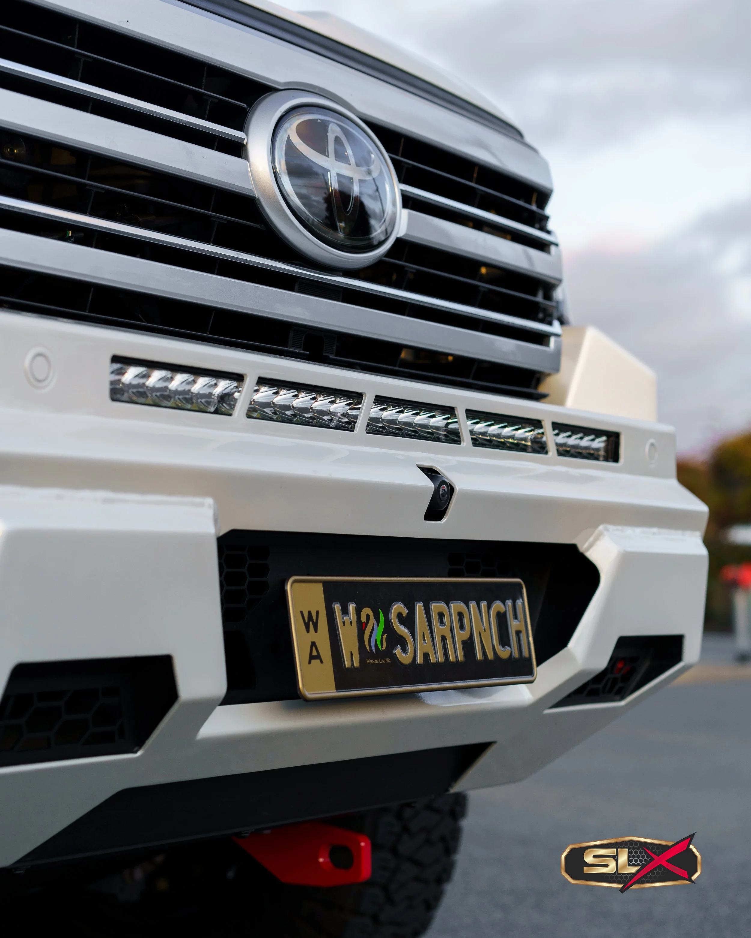 Close-up of the front grille and bumper of a white Toyota vehicle with a custom Australian license plate reading 'SARPNCH'.