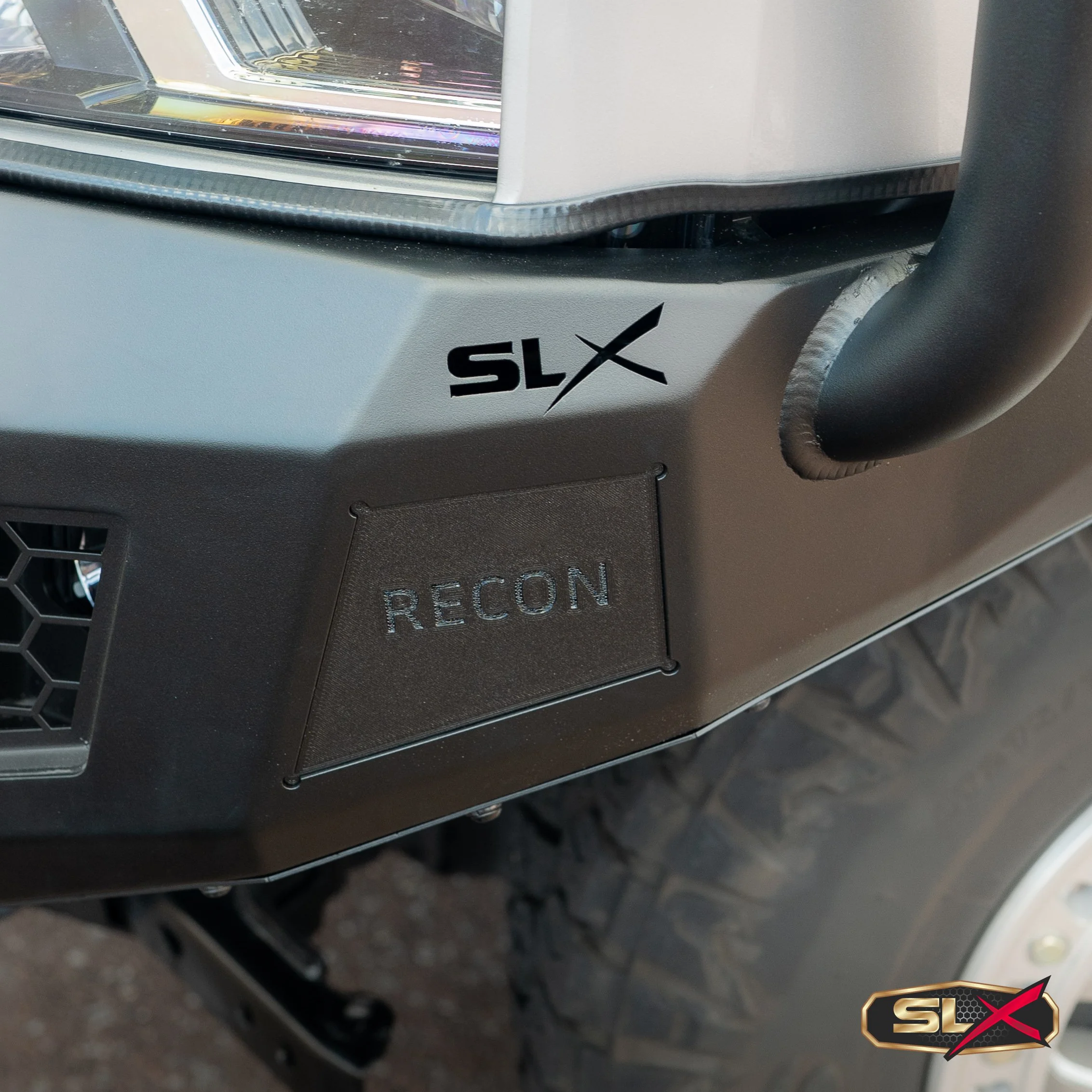 Close-up of a vehicle's front with an 'SLX' logo and a small black patch labeled 'RECON' on the black bumper area.