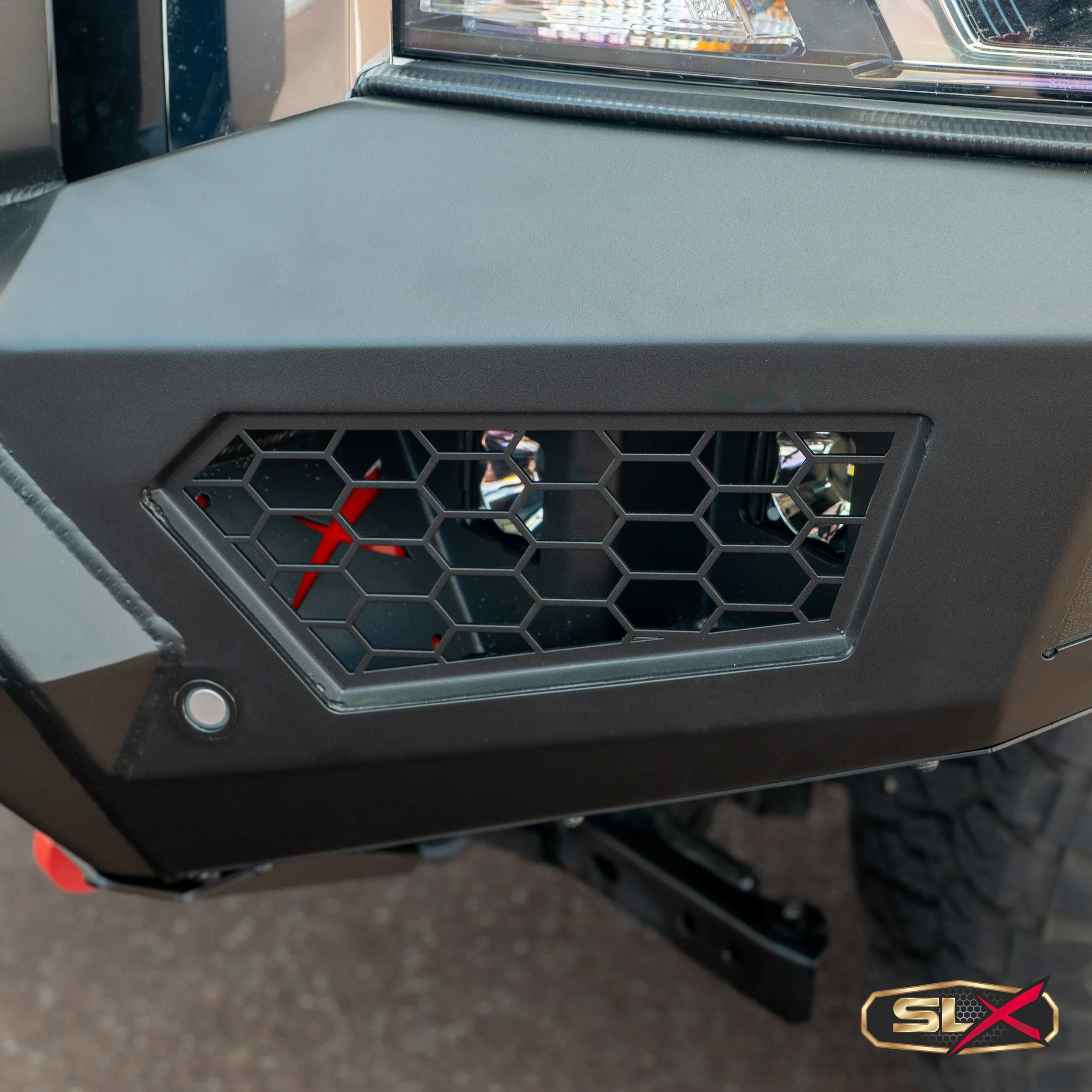Close-up of a side vent on a black vehicle, featuring a honeycomb grille and a red stylized design behind it, with a small circular button or indicator light nearby.