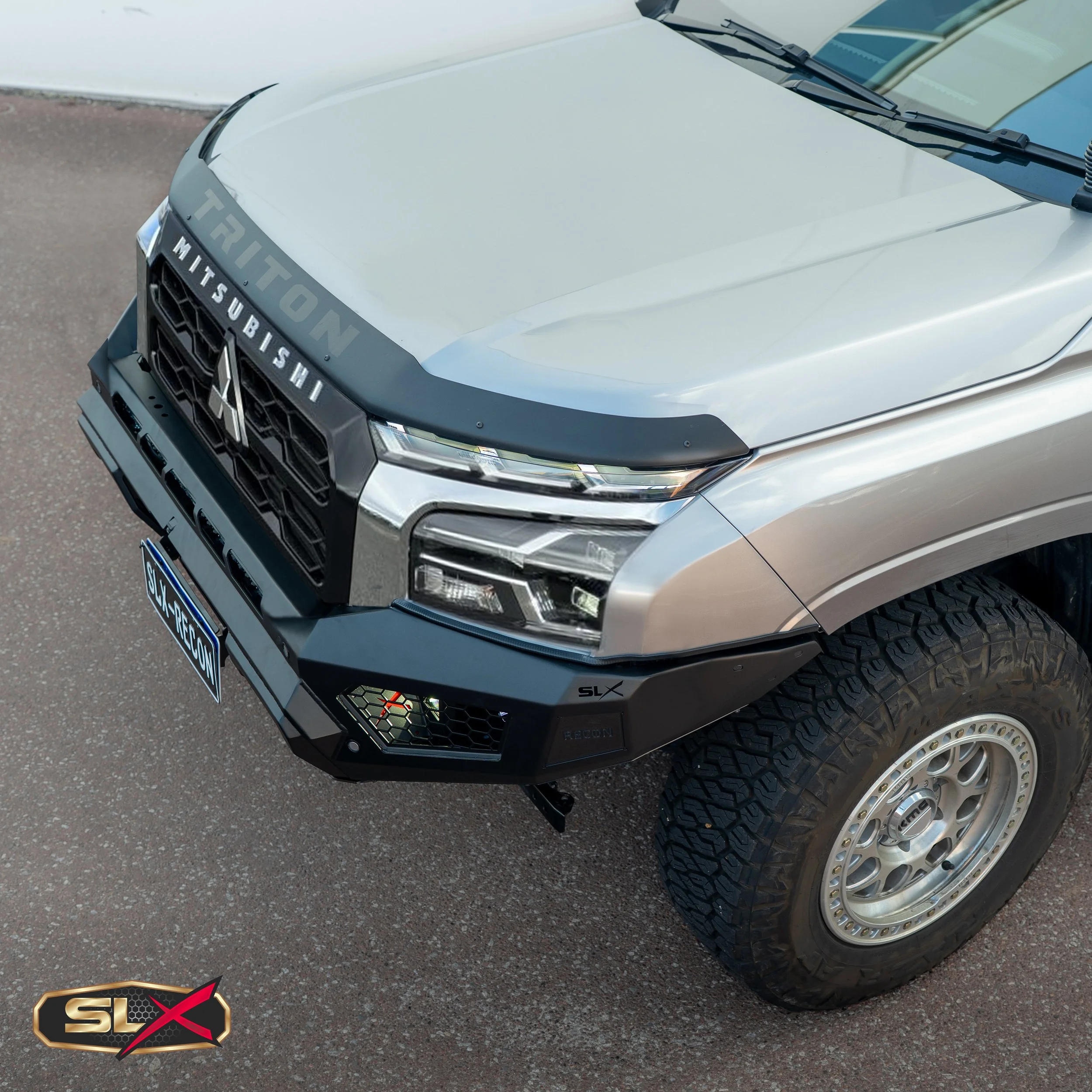 Front view of a silver Mitsubishi Triton pickup truck with a black RECON bumper and SLX badge, off-road tires, and Uber license plate.