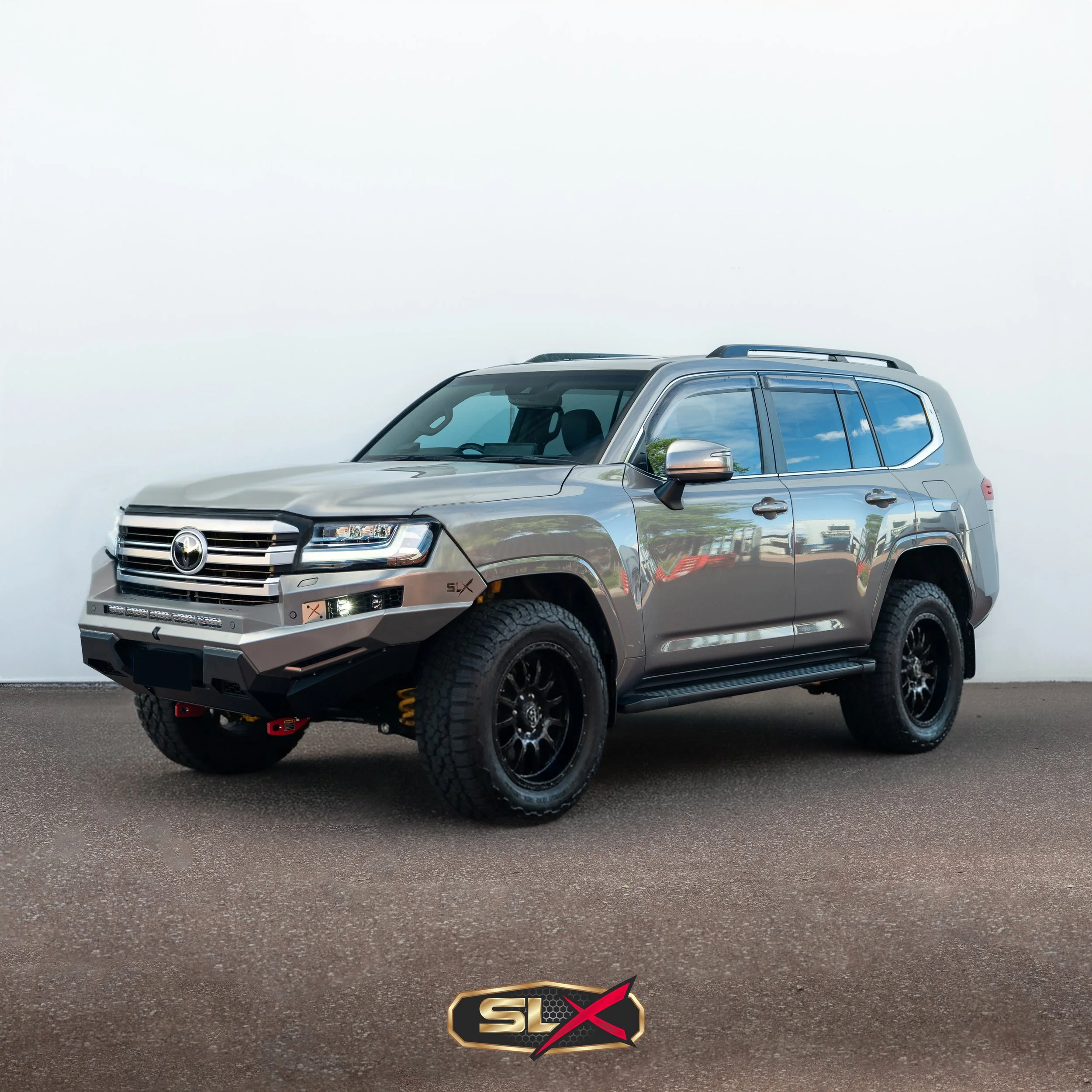 A silver Toyota SUV with black wheels parked indoors on a textured brown surface, with a plain white wall in the background.